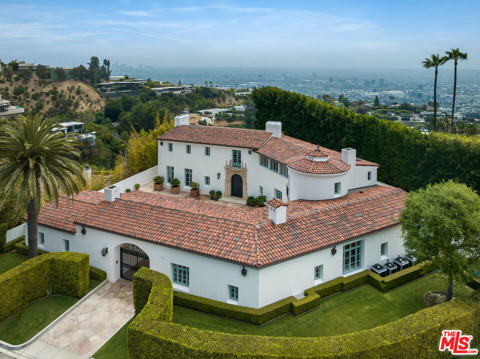 IMPECCABLE ATTENTION TO DETAIL AND NO EXPENSE SPARED ON THIS ICONIC MEDITERRANEAN VILLA LOCATED IN THE COVETED BIRD STREETS. A gated driveway leads you to a stunning courtyard and flagstone entry through monumental double doors framed in limestone. Inside, soaring 12-foot beamed ceilings, solid core doors, walnut, stone and marble flooring throughout. The main floor has a seamless flow, encompassing the living room, library, and a separate wet bar for entertaining. A formal dining room, butler's pantry, and a chef's kitchen with double sinks and exquisite appointments seamlessly connect to the family room, featuring another gorgeous fireplace. A guest suite, two powder rooms, and a separate laundry room offer both convenience and comfort, while a rotunda off the center hall adds architectural intrigue. Ascending the elegant stairwell to the second floor reveals the primary retreat. Here, a spacious sanctuary awaits, complete with a lounge area, wet bar, and 2 fireplaces. The expansive bedroom with his and her baths with luxurious soaking tub and French doors leads to triple Juliette balconies with sweeping city views. Two additional bedroom suites upstairs ensure ample accommodations for guests or family members. The lower level, off the rotunda, unveils further indulgence, including a third powder room, a cinema with a wet bar, and a temperature-controlled wine cellar adorned with built-ins. Throughout the home, quality casement windows invite natural light, while stone fireplaces add warmth and elegance. doors with designer hardware, along with beautiful plank walnut floors and perfectly curated marble and stone, elevate the interior to unmatched levels of sophistication. Outside, flagstone terraces envelop the home, creating an enchanting entertainment space adjacent to the infinity-edge pool, which overlooks the magical cityscape below. A three-car garage, clay tile roof, and expansive grassy area add practicality to the property's opulence, while substantial exterior lighting enhances its allure after dark. This estate is not just a home; it's a masterpiece of quality, design, and craftsmanship, meticulously curated with a highly sophisticated Crestron system throughout, ensuring effortless control of every aspect of modern living. With its unmatched blend of luxury, comfort, and technology, this property offers incomparable value for discerning buyers seeking California living in great style in the coveted Bird Streets.