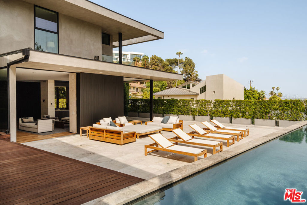 A true architectural masterpiece by HEH in collaboration with BO.SHI Architects, this private, design-forward residence offers the perfect balance of warmth, minimalism, and modern luxury just moments from the iconic Sunset Strip.Behind mature hedges and a gated motor court, enter through a dramatic 10-foot glass door into a stunning living and bar area featuring a floor-to-ceiling stone fireplace and expansive Fleetwood sliding doors. Designed for seamless indoor-outdoor living, the home features three striking stone fireplaces, including in the Primary suite, and a thoughtfully curated interior that exudes sophistication. The open-concept kitchen is a true showstopper, outfitted with Miele appliances and ideal for large-scale entertaining. The adjacent dining and family rooms flow effortlessly to the outdoor lounge with fireplace, swimmer's pool, and spa. A second outdoor retreat, lush and serene, sits just off the kitchenyour own private garden escape in the city. Upstairs, the luxurious Primary suite includes dual oversized walk-in closets, a spa-inspired bath wrapped in stone and marble, and panoramic views of Downtown LA. Two additional ensuite guest bedrooms, a sitting room, office, and laundry room complete the upper level. Additional highlights include a full-size home theater and bar, a lower-level guest suite, elevator access to all three levels, 5-car garage, and expansive motor court. Just a short distance to Sunset Plaza's top restaurants, shops, and nightlife--this is California living at its finest.