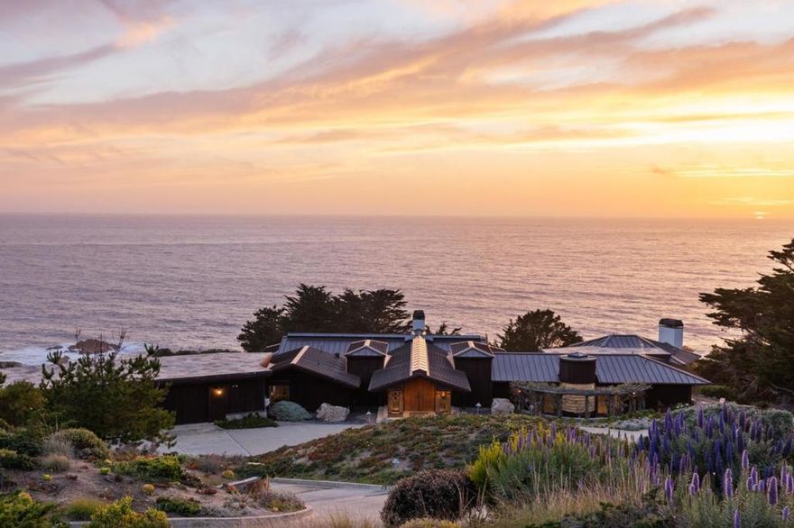 Modern elegance framed by coastal serenity. This exquisite four-bedroom, six-bathroom estate is nestled between the Santa Lucia Mountains and the Pacific Ocean, offering nearly six acres of privacy and sweeping views of the Carmel coastline. Sunlight pours through skylights and vast windows, illuminating a vaulted living room that flows into an elegant dining space. The gourmet kitchen features top-tier appliances, custom cabinetry, a sleek breakfast bar, and a cozy dining nook ideal for morning rituals. Step onto the wraparound balcony and breathe in the salt-kissed breeze as the ocean unfolds before you. The primary suite offers a gas fireplace, wood-clad ceiling, and a spa-like bath with cedar sauna and luminous glass block shower. A generous home office lies just beyond. Descend the spiral staircase to a recreation lounge with state-of-the-art theater, wine cellar, and wet bar. Two guest suites, each with private bath and walk-in closet, extend a warm welcome. A three-car garage, dual laundry rooms, and a private-access studio with kitchenette and bath complete this timeless sanctuary by the sea.