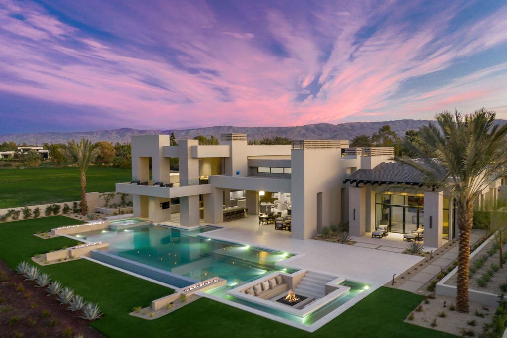 Designed by renowned architect Anton Marinkovich, this Desert Contemporary home boasts over 8,000 square feet, 5 bedrooms and five full and 2 half baths. Situated above the 5th hole of the Tom Fazio-designed golf course, it features west facing views of the majestic Santa Rosa mountains. A massive swimming pool nearly 80 feet in length adds a tanning shelf and swim up bar. Fire and water features are prevalent throughout, with nearly 7,000 sq. ft. of additional patio, courtyard and loggia space. A butler's kitchen highlights the entertaining spaces, while a media room upstairs has a five TV video wall. A sunken fire lounge accommodates a dozen guests as you serve from the glass wine wall which displays hundreds of your finest selections. The master suite welcomes you with a steam shower, his and hers showers, and a private whirlpool spa. Relax in the private zen garden as you bask in the grandeur of this beautiful estate.