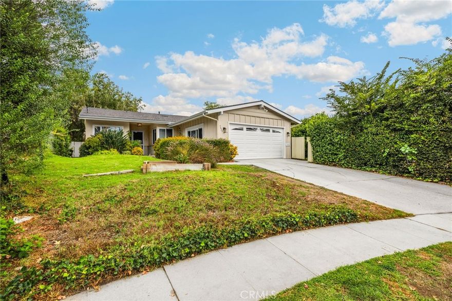 Nestled on a peaceful cul-de-sac in Valley Village, this charming single-level home offers 3 bedrooms, 2 bathrooms, and 1,727 sq ft of comfortable living space. Built in 1958, it features an attached two-car garage and a layout designed for ease and flow. Step through the front door and into the inviting living room, where rich wood flooring stretches across much of the home, setting a warm and cohesive tone. Just beyond, the formal dining area awaits—anchored by a cozy fireplace and illuminated by natural light pouring through a glass sliding door that opens to the backyard. The kitchen, conveniently located adjacent to the dining area, is equipped with ample cabinetry and a double oven, perfect for culinary enthusiasts. A quaint dinette area sits nearby, offering a lovely view of the front yard and a relaxed spot for morning coffee. Tucked between the kitchen and dinette is a discreet laundry closet, adding everyday practicality. Down the hall, two guest bedrooms provide restful retreats, each outfitted with ceiling fans for added comfort. A full guest bathroom serves these rooms, offering functionality and style. The primary bedroom suite is generously sized, featuring a walk-in closet and its own en-suite 3/4 bathroom with a shower, creating a private haven within the home. Step outside to discover a tranquil backyard framed by lush landscaping that enhances privacy. A covered patio invites outdoor dining, lounging, or entertaining in a serene setting. Located near award-winning schools, popular restaurants, and abundant shopping options, this home combines quiet residential living with convenient access to everything Valley Village has to offer.