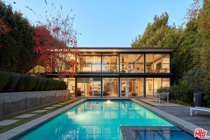 Situated on Alcima Avenue in Pacific Palisades, this tucked-back property exemplifies modernist design. Known as the "Abidi House," the residence exudes privacy and remains intact after the recent fires. Originally designed by acclaimed architect James Tyler (FAIA), former principal architect for Craig Ellwood, the home has been thoughtfully updated for contemporary living. Embracing its natural surroundings, the property features floor-to-ceiling windows in true mid-century tradition. The entry level opens with an expansive foyer framed by windows, leading to a great room that seamlessly combines living and dining areas, all oriented toward views of the backyard and pool. A covered outdoor dining terrace extends the living space, while two ensuite bedrooms and a gourmet eat-in kitchen complete this floor. The lower level offers the home's private quarters, including a serene primary suite, two additional bedrooms with a shared bath, and a flexible media room or indoor gym. Each generously sized room is thoughtfully designed to capture verdant outlooks and maintain a strong connection to the lush backyard. Outside, the centerpiece is a sparkling pool with a built-in spa, contributing to the property's calm, retreat-like atmosphere. Owners have completed all necessary remediation work resulting from the fires and will provide documentation to confirm.