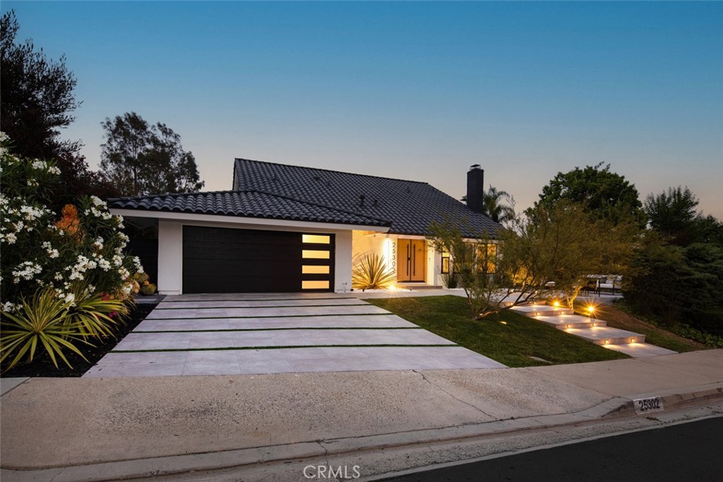 Poised atop a quiet Mission Viejo hillside, this newly reimagined residence reflects a considered balance between modern form and livable warmth. Thoughtfully redesigned to embrace its elevated setting, the home draws in natural light and expansive views while maintaining a grounded, calming interior palette. A refined materiality flows throughout, wide-plank oak floors, softly veined stone, and custom cabinetry create cohesion and visual stillness. The open-plan kitchen anchors the space with subtle sophistication, offering sculptural pendant lighting, minimalist shelving, and a seamless integration of function and style. Adjoining living and dining spaces are framed by full-height sliders that open effortlessly to a generous outdoor terrace, an extension of the home that blurs the threshold between indoors and out. The rear garden is equally intentional, a private and level expanse of green, edged by curated plantings and mature trees. This outdoor zone becomes a place of quiet retreat or casual gathering, all while orienting toward the soft hillside light and wide neighborhood vistas. Upstairs, the home’s private quarters are elevated in both placement and experience. The primary suite is enveloped in natural light, with carefully positioned windows framing views that shift with the time of day. Throughout, detailing is subtle and restrained, allowing the home's craftsmanship and connection to site to speak for itself. From the architectural entry path to its sculpted front façade and considered interior palette, this Mission Viejo residence offers a rare expression of refined minimalism where modern design is guided by simplicity, proportion, and place.