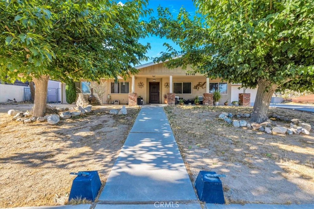 Welcome to your dream home in the beautiful Country Club area of Yucca Valley! This charming 3 bedroom, 2 bath home is nestled on just under 1/2 acre of meticulously landscaped grounds, offering the perfect blend of comfort and serenity. Upon arrival, you're greeted by a paved driveway leading to an attached 2 car garage, ensuring both convenience and ample parking space. Step onto the covered front porch and marvel at the stunning views. Inside, the expansive family room beckons with its large windows framing picturesque views and a cozy brick hearth fireplace, creating a welcoming ambiance. Soft carpeting underfoot adds a touch of luxury to this inviting space. The kitchen is a chef's delight, boasting tile countertops, stainless steel appliances, and abundant cabinetry for all your culinary needs. Adjacent to the kitchen, the dining room features a grand brick hearth with an indoor BBQ, seamlessly transitioning to the living room where you will find another fireplace on the side. The living room boasts beautiful wood beamed ceilings and French doors leading outside. Convenience meets functionality in the laundry room, complete with a second fridge for extra food and drink storage. The two guest bedrooms offer ample space and closet areas, while the guest bath features elegant tile countertops and a tiled tub/shower combo. Retreat to the generously sized primary bedroom, featuring its own attached bath for added privacy and comfort. Outside, the fenced backyard invites relaxation and entertainment with its breathtaking views, covered concrete patio, second brick patio, and a lush grassy area, perfect for kids and pets to play. With central heating and cooling ensuring year-round comfort, this home offers the ultimate in California desert living. Don't miss your chance to make this dream home yours! Schedule a showing to see this beauty for yourself.