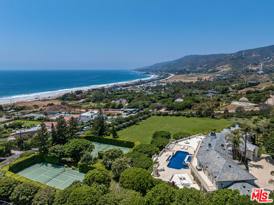 Coastal living at this rare and remarkable Malibu Mansion offers over 13,000 square feet of luxury on apprx. 5 versatile acres. Located a block from the Pacific Ocean, this estate is a quick walk to world-famous Zuma Beach, one of Malibu's most iconic stretches of sand, celebrated for its wide shoreline and ideal surf. Perfectly perched above the coastline capturing expansive, uninterrupted whitewater views of the Pacific Ocean from nearly every room. Sunrise to sunset, the crashing waves and endless horizon become a breathtaking part of daily life. Situated within prestigious Morning View Estates, some of Malibu's largest residences on oversized parcels, this grand property blends scale, comfort, and privacy. Inside are 8 en-suite bedrooms and 11 bathrooms, a gym, game room, and home theater, all designed for relaxed, elevated living. Sprawling Pacific Oceanfront decks anchor the outdoor lifestyle and flow seamlessly into an infinity-edge pool and resort-style jacuzzi that appear to spill into the sea. Among the estate's premier amenities are 2 full-size tennis courts, or can be used for pickleball, includes one of Malibu's only privately lighted courts for nighttime play. The grounds are equally captivating, with Italian-inspired gardens, a koi pond, cascading waterfalls, and over 30 mature fruit trees, creating a peaceful and picturesque setting. Separate guest or staff quarters offer added functionality and flexibility. Set across three legal parcels, the property offers significant opportunity for customization. Expansive flat land provides space to add equestrian facilities such as an arena, barn, and stables, ideal for a luxury horse property or refined farm setting. There is also room for a private sport court, golf hole, expansive orchard, or estate gardens, making this a truly multifunctional compound. Just minutes from Point Dume Village, Trancas Country Market, and Malibu's best restaurants and shops, with top-rated schools and the beach just a short walk away, this location combines everyday convenience with coastal privacy. Estates of this caliber, with over 13,000 square feet, nearly 5 acres of usable land, dramatic Pacific Ocean views, and convenient beach access - are exceptionally rare. This is one of the most significant offerings in Malibu's premier estate enclaves.