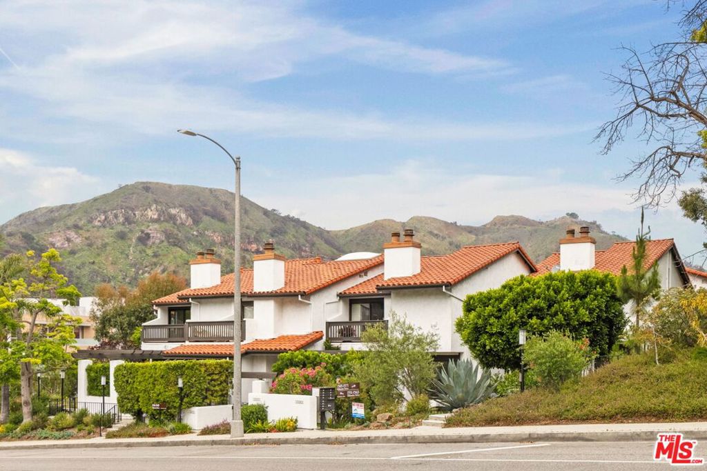 On the quiet curve of Palisades Drive, this expansive townhome unfolds with over 2,000-square-feet of natural light, volume, and functional design in the Palisades Highlands. A gated front entry leads to a dramatic interior where soaring beamed ceilings crown the main living room, anchored by a wood-burning fireplace and framed by sliding doors that open to a fenced terracotta patio ideal for al fresco dining or quiet evenings under the stars. The living room flows effortlessly up to a formal dining area and built-in bar with an elevated vantage point ideal for entertaining. The adjoining kitchen features stainless steel appliances including double wall ovens, a reverse osmosis water system, and a dedicated breakfast nook illuminated by soft morning light. Around the corner, a powder room completes the main level. Upstairs, the expansive primary suite is a true retreat, with vaulted ceilings, two generous walk-in closets, a spacious en-suite bath with dual vanities, and sliding glass doors that lead to a private balcony with mountain vistas. The upper level continues with two guest rooms and a second full bath, offering flexibility for guests, an office, and more. Additional highlights include an attached two-car garage with direct access, ample storage, and in-unit laundry. Recent upgrades include the HVAC system, dishwasher, and washer/dryer -- all completed in 2018. Residents enjoy exclusive access to a beautifully updated gym with a sauna, pool, and spa, surrounded by lush grounds and canopied hillsides. Set just moments from beloved local hiking trails and a quick drive from Palisades Village, 1559 Palisades Drive offers the ideal opportunity to live in one of the most sought-after enclaves on the Westside.