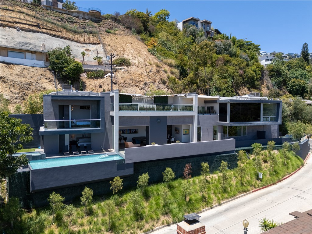 Introducing Stebbins Terrace — a landmark architectural estate nestled in the hillside of Lower Sunset Plaza. Designed with intention and precision by Melanie Mar Design, this custom-built residence blends bold form with refined livability, offering sweeping city views from nearly every room. Privately situated at the end of a quiet cul-de-sac, just minutes from the Sunset Strip, the home offers the rare balance of tranquil seclusion and immediate access to LA’s premier cultural and dining destinations.
Inside, dramatic scale meets thoughtful refinement. Soaring ceilings and walls of glass frame sweeping skyline vistas, while Fleetwood pocket doors fully retract to create seamless indoor-outdoor flow. A chef’s kitchen, expansive living areas, and open-concept design set the stage for effortless entertaining.
Step outside to an entertainer’s dream: a saltwater infinity pool suspended above the city, a fire-lit dining terrace, and a 700 sq. ft. covered deck with a built-in bar and fire pit — all set against a backdrop of glittering city lights.
Smart home features include automated controls for the gated entry, fireplace, pool, and full Sonos sound system. First time available in nearly a decade, this is a rare opportunity to own one of Sunset Plaza’s most iconic modern homes — where privacy, design, and view converge in a truly elevated living experience.