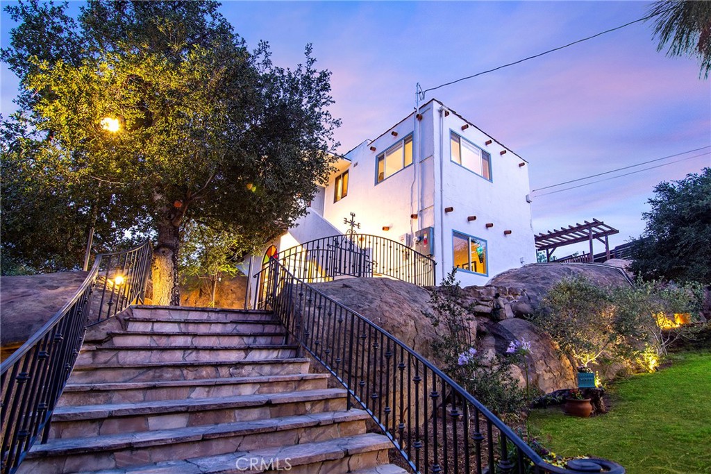 Hollywood Hills charm meets tranquil canyon living in West Hills. This one-of-a-kind Spanish adobe home is perched atop a sandstone ridge, offering unobstructed 360-degree views of the entire San Fernando Valley. Inside, you’ll find 3 bedrooms and 3 full baths across an open-concept floor plan featuring vaulted ceilings with exposed wood beams, creating a warm and airy ambiance.
Enjoy seamless indoor-outdoor living with expansive sliding glass doors that open to a wraparound deck, sun deck, and a stylishly integrated above-ground pool with custom wood decking—perfect for relaxing, entertaining, or cooling off beneath the trees. The charming yard and sitting areas offer peaceful spaces to unwind while soaking in canyon and valley views.
Modern upgrades include solar panels, a 200-amp electrical panel, landscape lighting, and a dedicated electrical panel by the pool. The property is fully fenced with dense Mangaris wood, and includes two sheds for extra storage, a one-car detached garage with carport, and ample parking.
Smart home features include five Ring security cameras, a remote-controlled thermostat, and a WiFi-enabled deadbolt at the front gate, all easily managed from anywhere. Set at the end of a quiet, no-through street, this home offers ultimate privacy, European character, and direct access to incredible hiking trails.
Other highlights include a mesh Wi-Fi system indoors and out, majestic oak trees, and the convenience of a main sewer connection (no septic). This rare architectural retreat seamlessly blends character, nature, and modern amenities.