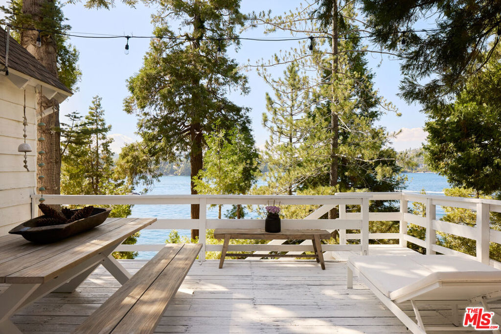 Architectural lakefront sanctuary with uninterrupted views of the lake from every room. Located in the sought-after Palisades neighborhood, this meticulously designed home offers lake rights and direct access to a deep-water single-slip dock and dock house with electricity, situated directly below the property. A deep commitment to design integrity guides the refined material palette and deliberate selection of finishes that distinguish the home from the expected. Disciplined detailing defines the interior, where white oak floors, custom-built European cabinetry, imported marble and travertine surfaces, and designer fixtures combine to create a carefully curated balance of texture and tone. The living room features vaulted ceilings with exposed wood beams and expansive glass sliders that flood the space with natural light and open to a generous lake-facing deck, seamlessly connecting indoor and outdoor areas. The chef's kitchen, outfitted with a Viking range, hood, dishwasher, Fisher & Paykel refrigerator, and polished Negro Marquina marble countertops, extends to the dining room with wraparound windows overlooking the lake. A tranquil, main-level primary suite of grand proportions features beamed ceilings, abundant natural light, and unobstructed views of the lake and surrounding mountains, underscoring the home's strong connection to its natural setting. The ensuite bath includes Ocean Silver Travertine slab countertops and dual vanities, continuing the thoughtful material palette. Four secondary bedrooms are sensibly distributed throughout the home. On the upper level, a sizeable guest room captures picturesque lake views, while a cheerful bunk room offers a convenient option for additional guests. Two more guest rooms on the lower level enjoy lake views and open to a secluded secondary patio just above the trail. Completely private yet visually connected to the water and dock house below, the patio serves as a peaceful retreat or versatile entertaining space. With a spacious two-car garage, additional off-street parking, and a gentle, unobstructed approach from the street, the property is as functional as it is beautiful. Located just minutes from the village yet tucked away from foot traffic and noise, this home offers immediate access to Lake Arrowhead's most desirable amenities while preserving the serenity of a private retreat.