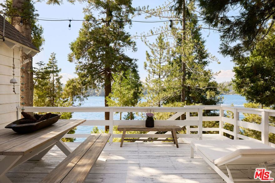 Architectural lakefront sanctuary with uninterrupted views of the lake from every room. Located in the sought-after Palisades neighborhood, this meticulously designed home offers lake rights and direct access to a deep-water single-slip dock and dock house with electricity, situated directly below the property. A deep commitment to design integrity guides the refined material palette and deliberate selection of finishes that distinguish the home from the expected. Disciplined detailing defines the interior, where white oak floors, custom-built European cabinetry, imported marble and travertine surfaces, and designer fixtures combine to create a carefully curated balance of texture and tone. The living room features vaulted ceilings with exposed wood beams and expansive glass sliders that flood the space with natural light and open to a generous lake-facing deck, seamlessly connecting indoor and outdoor areas. The chef's kitchen, outfitted with a Viking range, hood, dishwasher, Fisher & Paykel refrigerator, and polished Negro Marquina marble countertops, extends to the dining room with wraparound windows overlooking the lake. A tranquil, main-level primary suite of grand proportions features beamed ceilings, abundant natural light, and unobstructed views of the lake and surrounding mountains, underscoring the home's strong connection to its natural setting. The ensuite bath includes Ocean Silver Travertine slab countertops and dual vanities, continuing the thoughtful material palette. Four secondary bedrooms are sensibly distributed throughout the home. On the upper level, a sizeable guest room captures picturesque lake views, while a cheerful bunk room offers a convenient option for additional guests. Two more guest rooms on the lower level enjoy lake views and open to a secluded secondary patio just above the trail. Completely private yet visually connected to the water and dock house below, the patio serves as a peaceful retreat or versatile entertaining space. With a spacious two-car garage, additional off-street parking, and a gentle, unobstructed approach from the street, the property is as functional as it is beautiful. Located just minutes from the village yet tucked away from foot traffic and noise, this home offers immediate access to Lake Arrowhead's most desirable amenities while preserving the serenity of a private retreat.