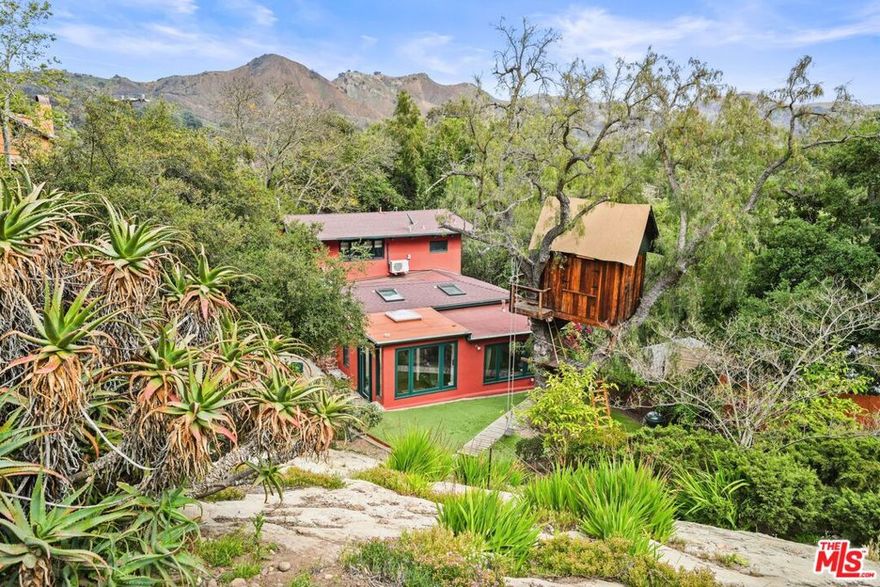 Welcome to Fairy Land. Hidden behind gates, Haven Villa is your secret paradise on a quiet street in Fernwood. This graceful property is set in magical, boulder-strewn gardens. Breathe deeply; bright flowers, native plants, and fruit trees tumble across the bold rock formations, scenting the cool coastal breezes. Enter through doors flung open to spacious patios, a flat yard, and a sunken courtyard. Craftsman and French country touches mingle to up the ante on the charm. Wood-paneled ceilings, wide view windows, and a massive handbuilt, petrified stone fireplace draw you into the wide open living room. Rooms flow effortlessly across gleaming oak floors. The exquisite newer kitchen, with honed Soapstone counters, high end appliances, and a farmhouse sink is open to the generous dining room. Enjoy your guests, your view of the mountains, and your windowed pantry, as you while away the hours in culinary creativity. You'll mostly use the dining room entry, but the mudroom has a wide window seat with huge windows looking out over the verdant yard and the 3 story Swiss Family Robinson tree house, with a sleeping loft and operable skylights. Curl up with a good book and watch the birds flit amongst the greenery. You'll be distracted by the mountain views from your bright, main floor office. Upstairs the primary suite beckons. High-beamed ceilings shelter, and a wall of custom built closets are topped by clerestory windows, bringing in the sky. The air conditioning holds the summer heat at bay. Sunshine pours into the remodeled bathroom suite. A shower room built for 2, with a long teak bench, is to one side. Turn it into a blissful sauna with the steam bath feature. The water closet is to the other side with a built-in bidet with a heated seat to up the comfort. The wide room in between has a dual vanity, a linen closet, and canyon views. Downstairs, 2 more bedrooms, a laundry, and an updated full bath round out the main house. Stone paths, steps, and walls wend through the rugged landscape. A large entertaining deck perches nearby, shaded by a wood pergola, wisteria, and bougainvillea. Nestled near the top of the property, a studio guest house with kitchen, bath, and wood burning stove, basks in cross canyon views. Nearby a viewing spot with Adirondack chairs awaits in the shade of an old pepper tree. Drink your morning coffee or sip your cocktail as you watch the Dragon's Breath fog move up through the canyon. A fully enclosed raised-bed garden protects the tomatoes and basil from the critters. A shed sits nearby to hold all of the garden tools. There is a carport. At night, landscape and deck lighting enhance the magic for entertaining, creating an evening fairy land. Everything is nearby: the center of the canyon with shops and cafes, the parks and trails, the beach, Malibu, the valley, and the wider city. You can take off to anywhere from here. But here is as wonderful as anywhere else you might go. Stay a while.