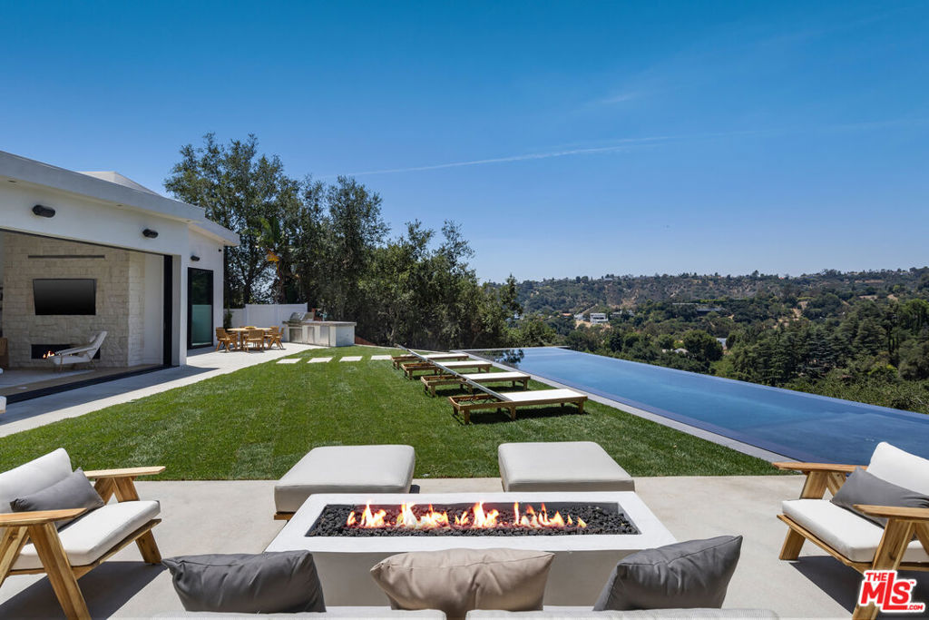 Tucked away on a quiet cul-de-sac in the prestigious Beverly Hills Post Office area, this newly completed modern masterpiece offers breathtaking jetliner canyon views. Privately gated for maximum security and seclusion, the home showcases soaring 18-foot mahogany-clad ceilings, multiple skylights, a dramatic 16-foot-tall library, and expansive sliding glass doors for seamless indoor-outdoor living. The dramatic black-tiled pool, perched on five structural caissons, features a stylish Baja shelf - perfect for lounging in privacy while enjoying the view. Distinctive interior finishes include white oak flooring, Calacatta Cremo countertops in the kitchen, Fantasy Pink marble vanities in the guest suites, and a powder room with Calacatta Picasso marble and Roman clay walls. Custom walnut cabinetry adds warmth and sophistication throughout. The primary suite features a serene sitting area, a large custom walk-in closet, and a spa-like bath with a soaking tub overlooking the stunning views. Outdoors, enjoy a full kitchen equipped with a sink, BBQ, and refrigerator, along with a built-in fire pit perfect for entertaining. Every detail has been thoughtfully curated to elevate both design and function. With world-class finishes and exceptional craftsmanship, this home is a true expression of luxury living.
