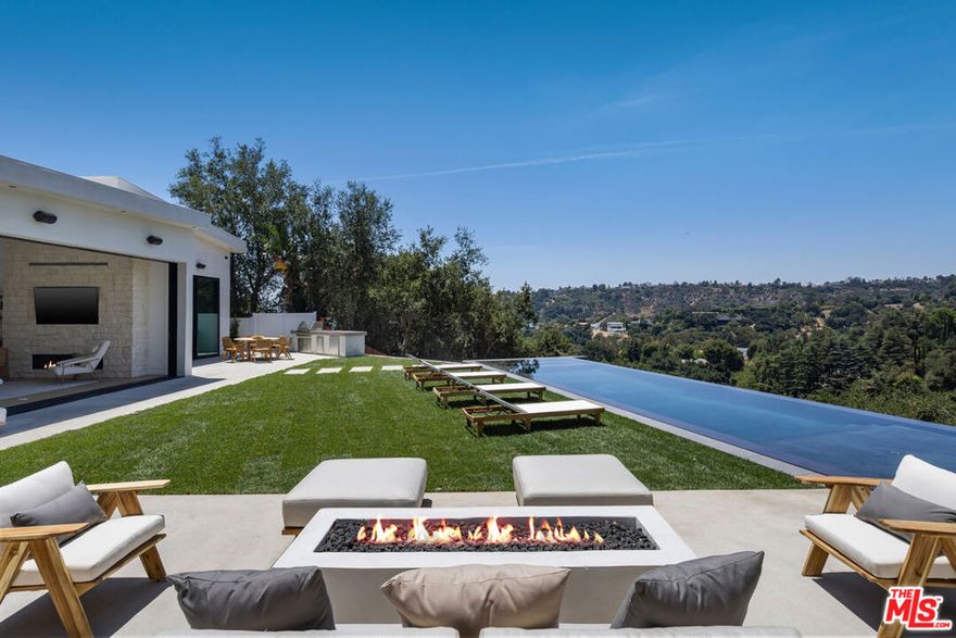 Tucked away on a quiet cul-de-sac in the prestigious Beverly Hills Post Office area, this newly completed modern masterpiece offers breathtaking jetliner canyon views. Privately gated for maximum security and seclusion, the home showcases soaring 18-foot mahogany-clad ceilings, multiple skylights, a dramatic 16-foot-tall library, and expansive sliding glass doors for seamless indoor-outdoor living. The dramatic black-tiled pool, perched on five structural caissons, features a stylish Baja shelf - perfect for lounging in privacy while enjoying the view. Distinctive interior finishes include white oak flooring, Calacatta Cremo countertops in the kitchen, Fantasy Pink marble vanities in the guest suites, and a powder room with Calacatta Picasso marble and Roman clay walls. Custom walnut cabinetry adds warmth and sophistication throughout. The primary suite features a serene sitting area, a large custom walk-in closet, and a spa-like bath with a soaking tub overlooking the stunning views. Outdoors, enjoy a full kitchen equipped with a sink, BBQ, and refrigerator, along with a built-in fire pit perfect for entertaining. Every detail has been thoughtfully curated to elevate both design and function. With world-class finishes and exceptional craftsmanship, this home is a true expression of luxury living.