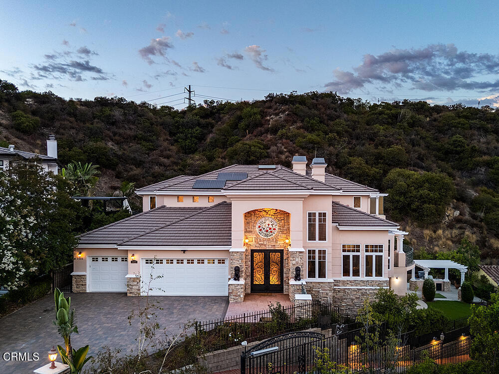 Perched high in the hills above Glendale, this custom-built 1998 residence showcases sweeping views of the lower basin and sparkling city lights. Designed with scale and sophistication, the home offers 5 bedrooms, 5 bathrooms, and two kitchens, along with an array of refined living and entertaining spaces.Spanning three levels, the floor plan blends intimacy with grandeur. Highlights include a wood-paneled library with wall-to-wall bookcases and dramatic views, a formal dining room, and a welcoming family room with a broad balcony overlooking the city. The living room is accented with Venetian plaster walls and an artist-designed stained-glass depiction of Springtime above the entry door, creating a striking first impression.At the heart of the home, the main kitchen features an oversized granite island, custom-designed cabinetry, and state-of-the-art appliances, including a Sub-Zero refrigerator/freezer, Wolf range/oven, and Bosch dishwasher. An additional kitchen offers versatility for entertaining or multigenerational living.The oversized primary suite enjoys its own view balcony and a luxurious bath with separate tub and shower. On the lower floor, an ensuite bedroom and versatile entertainment room open seamlessly to the gardens, offering an ideal indoor-outdoor flow.Outdoors, the grounds are designed for year-round enjoyment with lush landscaping, a covered patio, built-in BBQ, and tranquil gardens. A newly paved driveway enhances the home's curb appeal, while a solar power system provides modern efficiency.Inside, the extensive use of marble, granite, wood, and glass creates a timeless sense of opulence--equal parts warm and dramatic. Sited at the end of a cul-de-sac, this property offers both privacy and prestige.This is more than a home--it is a statement of elegance and comfort, perfectly suited for intimate living or large-scale entertaining, all set against a backdrop of panoramic vistas.