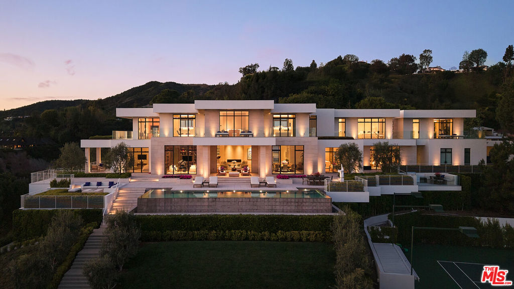 Set high in the hills above Los Angeles, this newly completed Beverly Hills estate represents six years of precision planning and expert craftsmanship, framed by sweeping 180-degree southern views that stretch from the Pacific Ocean to the shimmering city skyline. 9966 brings together best-in-class materials, advanced systems, and resort-caliber amenities across three thoughtfully designed levels, resting on more than two and a half acres of manicured grounds. Through a gated drive and behind custom steel-framed doors awaits 15,700 square feet of meticulously crafted living space, featuring rare rift-sawn white oak flooring, a limestone fireplace, and oversized custom windows that flood the home with natural light. The Bulthaup-designed kitchen is outfitted entirely with Gaggenau appliances, while a Crestron-controlled environment seamlessly manages the home's audio system. A climate-controlled wine room with display shelving for up to 640 bottles serves as both a collector's showcase and an architectural focal point. In addition to the interior living space, the estate offers more than 7,200 square feet of outdoor terraces, designed for dining, lounging, and entertaining against a stunning backdrop of sweeping views. A sculptural staircase and elevator lead to the upper floor, where the primary suite features dual bathrooms, dual walk-in closets, and commanding panoramic vistas. Additional spaces include multiple guest suites, a glam room, art studio, massage room, full gym, and an acoustically engineered Dolby Atmos theater. A 23-zone RVR HVAC system by Daikin provides precision climate control, allowing every room to maintain its own ideal temperature. Outdoors, the amenities continue with a 52-foot pool, private tennis court, and carefully maintained green spaces. Rarely does a property in Beverly Hills offer this level of infrastructure, privacy, and architectural clarity, making 9966 a true testament to timeless luxury and modern design.