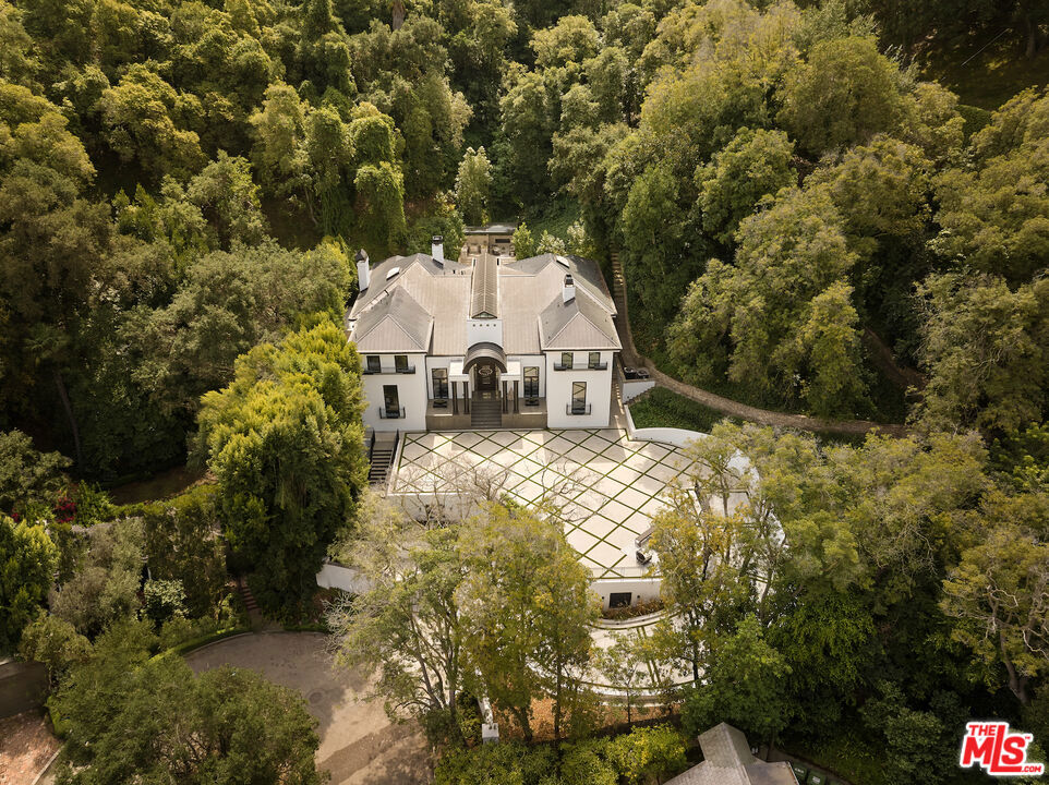 Completely private and set behind gates, a reimagined Bel Air estate with over an acre of lush grounds, a long private driveway and a 12 car auto gallery. The arrival sequence unfolds with a grand entry and sweeping staircase beneath soaring ceilings, where walls of glass and skylit atriums cast shifting patterns of light and shadow throughout the day. A sculptural second-floor walkway overlooks the pool terrace, leading to an open lounge that feels suspended among the treetops, an architectural gesture that blurs the boundary between indoors and out. At the heart of the home, the chef's kitchen features dual islands, dual ovens, dual dishwashers, a professional range with pot filler, and an integrated suite of Thermador appliances. Multiple gathering areas provide flexibility for both entertaining and daily living, while a stately wood-paneled office channels the gravitas of a presidential study. The primary suite spans two distinct wings, each with its own walk-in closet and spa-like bath featuring soaking tub, rainfall shower, and double vanities. Secondary bedrooms and flexible spaces are designed for family, guests, or creative pursuits. The outdoors unfold as a private entertaining haven. A geometric stone-and-grass terrace frames the pool, bordered by three fireplaces stretching across the length of the elevated wall. Above, a pavilion with full kitchen, bar, and trellised lounge creates the ultimate alfresco setting. Beneath it all, a nearly 2,500 sqft garage offers the scale and security to showcase a collection. Nestled within one of Bel Air's quietest cul de sacs, 10640 Taranto Way offers a sense of retreat while remaining moments from Hotel Bel-Air and Bel Air Country Club. Its hillside position ensures seclusion, yet easy access to Sunset Boulevard and canyon roads makes the entire city readily accessible.