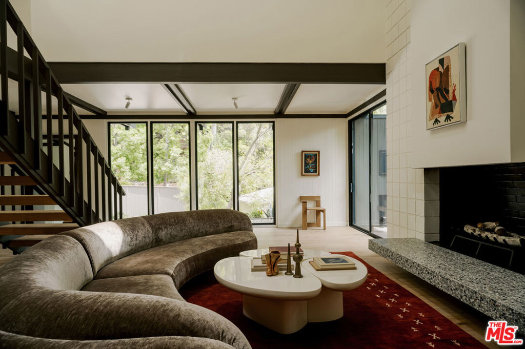 Can a home make it feel like you're living inside a '60s architectural magazine spread? With this stunning residence set on a secluded cul-de-sac in the Los Feliz Oaks, the answer is an emphatic yes! Redesigned by acclaimed Working Holiday Spaces, this two-story retreat is an inspired homage to mid-century modernism: clean lines, organic textures, and all the poetic simplicity of a Case Study House without being one. Dark exposed beams trace the lofty ceilings, drawing your eyes across luminous white walls and floor-to-ceiling windows that invite the hillside foliage indoors. The double-height living area showcases the vintage vibe with a soaring tile-backed fireplace and floating hearth, flowing effortlessly into the dining alcove and outside to a serene seating corner, where steps rise to your layered backyard sanctuary. A sculptural open-riser staircase anchors the interior like functional art. The kitchen is a masterclass in design; natural light streams through oversized skylights onto sleek marble countertops, an expansive island, integrated high-end appliances, a banquette breakfast nook, and custom wood cabinetry. Track lighting and warm wood floors guide you throughout, adding a timeless touch. With 3 bedrooms, 3.5 baths, and a den that flexes as an office or guest accommodations, the layout is intentional for maximum versatility. Every bath impresses with extensive tilework and custom cabinetry, including your primary's ensuite with its dual vanity. Upstairs, sliding glass doors reveal a flagstone patio ideal for peaceful morning coffee and evening cocktails, while a generous deck awaits for alfresco entertaining. A spacious laundry room and driveway parking complete the conveniences. Just minutes from Griffith Park, the 101, and the cultural buzz of Hollywood, opportunities like this don't just pop up; they're crafted. Come see where good design can take you!