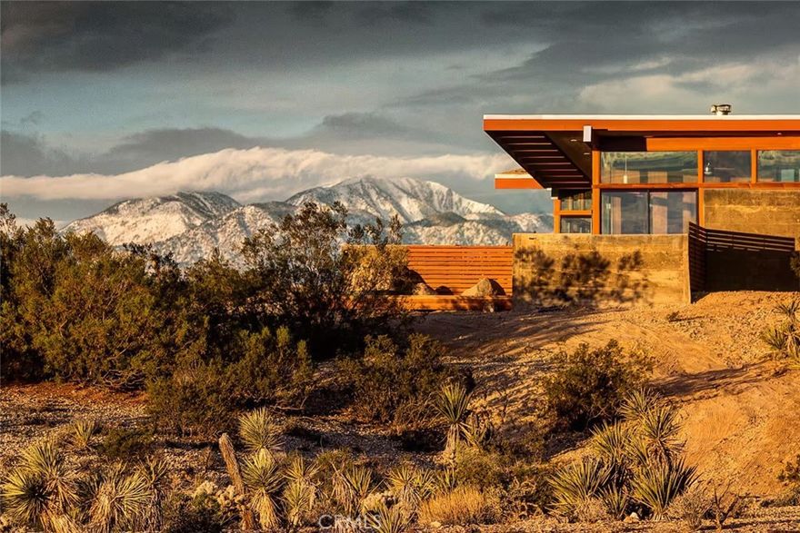 The New Joshua Tree: Premier architectural masterpiece designed and hand-built over nearly a decade (2004-2012) by a Harvard trained architect. Midcentury influence with modern green sensibilities, including radiant heated concrete floors, passive solar design for low heating/cooling costs and floor to ceiling windows throughout for abundant natural daylight. Handmade custom cabinetry and casework made of clear vertical grain Douglas fir wood. Abundant closet/storage space along entire north wall of the house. Formed concrete walls throughout. Beautifully designed entry foyer. Intimate nighttime views of downtown Joshua Tree in the distance and expansive daytime views of Joshua Tree National Park and surrounding mountains from all rooms. Secluded and tranquil location, yet convenient to town. Swimming pool enclosed on private deck. Property sits on border of Yucca Valley & Joshua Tree – adjacent parcel to east has a Joshua Tree address. Operated as exclusive vacation rental with successful rental history. Property is being sold as a rare architectural achievement for the local area. Shown by advanced appointment only. Loan Prequalification Letter or Proof-of-Funds required to show.