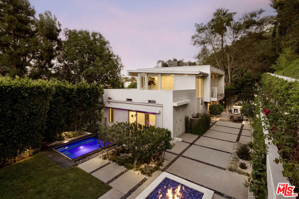 Located at the top of the Hollywood Hills, this sophisticated home offers sweeping views and sleek, serene living. Privately tucked behind lush greenery, it embodies the ultimate California lifestyle. Expansive floor-to-ceiling windows frame iconic vistas of the Hollywood Sign, city lights, and tranquil canyons, filling every room with beautiful natural light. The first level features an open-concept living space with a custom-built kitchen, creating a perfect centerpiece for living and entertaining. You'll also find a laundry area, guest bathroom, and a versatile bedroom ideal as a guest suite or home office.Upstairs, surrounded by windows, are two additional bedrooms, including a primary suite with a private terrace overlooking the hills, an ensuite bath, and a walk-in closet. This level also offers an expansive deck for lounging, entertaining, or taking in the views. Throughout the home, thoughtful details shine, such as French white oak floors, steel-framed doors, and top-tier appliances, all designed to elevate both style and comfort. Indoor-outdoor living is seamlessly integrated, with exterior spaces that include an oversized spa with a cascading waterfall, a built-in fire pit, and a fully equipped outdoor kitchen and dining area.With a gated two-car garage and additional parking, the property offers both beauty and ease. Just minutes from Runyon Canyon and with easy access to both sides of the hill, it is a private sanctuary at the center of it all.
