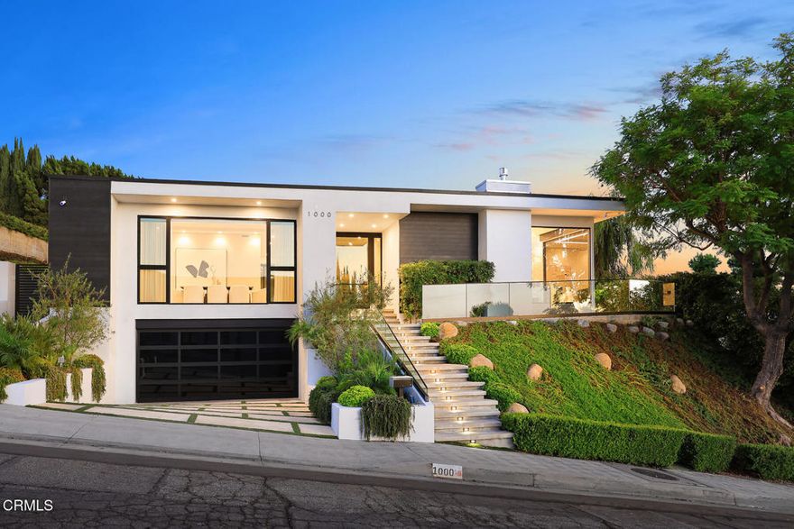 Introducing 1000 Avonoak Terrace, a Stunning Contemporary Villa with panoramic views stretching from the skyline of downtown Los Angeles to the mountains of Glendale. Perched on an elevated lot in the prestigious enclave of College Hills, this architectural gem was thoughtfully remodeled and expanded in 2022, blending modern sophistication with organic warmth & texture, showcasing a timeless design elevated by curated materials and high-end designer finishes throughout. Experience soaring 10-foot ceilings and floor to ceiling windows in the main living areas creating an atmosphere bathed in soft natural light. The 9-foot custom steel and glass front door makes a dramatic first impression entrance. A skylight illuminates a grand front entry leading to the spacious living room w/ fireplace & sweeping views, flowing seamlessly into a formal dining area and an open concept family room which interacts with the kitchen and has views to the living room. The kitchen is anchored by Thermador and Miele appliance suites, designed to elevate the culinary experience, including a wine cooler, coffee/espresso system, Perlick dual-drawer refrigerator, heated water dispenser, and seamless European cabinetry, accented by waterfall stone countertops, and a sit-up island complete the space. Featuring three luxurious ensuite bedrooms and four bathrooms - the primary suite, framed by stunning views, offers a serene spa-inspired bathroom, his/her custom walk-in closet, and a private balcony. Two secondary ensuite bedrooms w/beautifully designed 3/4 baths, custom closets, w/ views and access to outdoor patio and courtyard spaces. Step into a beautifully landscaped courtyard retreat. Offering a built-in outdoor kitchen w/ an expanded granite waterfall countertop, Lynx barbecue and integrated cooktop, generous dining, and lounge area w/ a modern gas fire pit --perfect for intimate evenings or entertaining guests. Indulge in the private outdoor spa, set against sweeping skyline & mountain views, and explore the wraparound patio with glass railings--all thoughtfully designed for seamless indoor-outdoor living. Additional highlights - automated window shades, flush-mount dimmable lighting, landscaping w/ driplines, home security system, dual-zone HVAC w/Nest, 400-amp electrical service, tankless water heater, EV charging station in garage and bonus storage room. Come experience this one-of-a-kind luxury home - a perfectly composed sanctuary where luxury meets lifestyle.