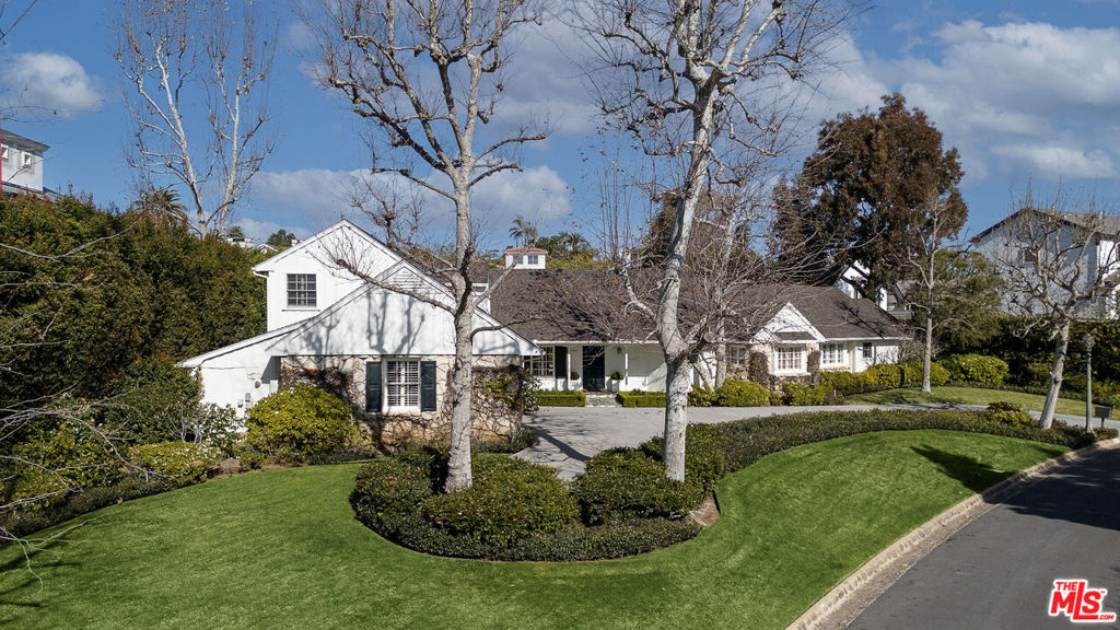 Nestled in the highly sought-after Riviera neighborhood and making its debut after four decades, this exquisite Traditional ranch includes wonderful architectural details, views, light-filled rooms, and a flat rear yard with mature hedges for privacy, large grassy areas, multiple dining patios, and beautiful pool/spa. With five bedrooms total two on the first floor plus a bonus room off the kitchen and two upstairs in a separate wing off the kitchen - the floor plan offers flexibility and privacy. The inviting great room combines the formal living room with a fireplace, built-in bookshelves, French doors to the backyard, and a beautiful circular dining area with a wall of windows. Off the living room is a cozy den/library with built-in bookshelves. The primary bedroom has panoramic views across the canyon, dual walk-in closets, a spa-style bathroom, and a dedicated office. An adjacent en suite bedroom with a large closet also offers views. The gourmet kitchen and family room have soaring cathedral ceilings, a fireplace, French doors, a center island/breakfast bar, and temperature-controlled wine storage. Off the porte cochre is a two-car garage and a separate storage/work room. This property epitomizes the perfect blend of sophistication, comfort, and versatility, offering a unique opportunity to experience the epitome of Riviera living.