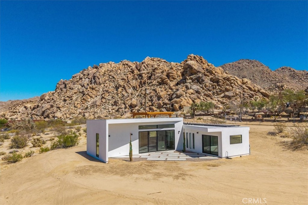Spectacular New Construction Design & Location: Walking distance to Joshua Tree National Park – leave car at home and hike or jog into the vast wilderness only minutes away. In addition to the close proximity of nature, and only one parcel away, stands Joshua Tree’s most significant architectural jewel – The Kellogg Doolittle House, built into the boulders. Few local properties can boast such an iconic neighborhood structure and the freedom to roam at will on protected land. Sited at the base of a boulder mountain sits this beautifully designed home with a sunken living room, polished concrete floors, clean lines and numerous windows with stunning views in every direction. The kitchen features an island with double-waterfall quartz counters, subway tile backsplash and a window above the sink that perfectly frames the boulders above. Zoned ductless mini-splits allows for efficient cooling and heating. Floor-to-ceiling tile in the bathroom. Each bedroom has its own large sliding glass door for indoor/outdoor living. This is the second home the owners have built in prestigious Panorama Heights in South Joshua Tree. The first home is a high-grossing Airbnb that was featured in Architectural Digest, with a similar L-shaped design. However, this new property features a more spectacular and coveted location. Views to the west include SoCal’s tallest mountain – San Gorgonio – and sublime sunsets. No through traffic, as road ends only a few away near the National Park boundary. Also included are plans for a pool that are pending approval (for buyer to build at a later date if desired.) Whether looking for a primary residence or a vacation home investment, few properties share the qualities of this unique home and location.