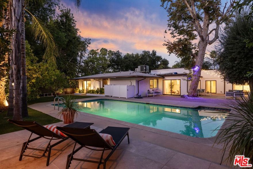 Welcome to Caritina Estates, a hidden mid-century gem and tranquil haven nestled in a secluded cul-de-sac just south of the boulevard in Tarzana. This exquisitely updated single-story residence commands attention with its 2,702 square feet of refined and elegant living space, set upon a sprawling 18,904 square foot lot. The home is masterfully designed to offer both comfort and contemporary luxury, featuring four spacious ensuite bedrooms, including two sumptuous primary suites. The residence's intelligently crafted layout harmonizes functionality with style, featuring warm hardwood floors that seamlessly guide you through the main living areas. In contrast, the kitchen and bathrooms are adorned with sophisticated ceramic and tile flooring, elevating the home's aesthetic appeal. At the heart of the home lies the Chef's Kitchen, a culinary dream equipped with a built-in refrigerator, sleek Ceaserstone countertops, and a modern backsplash and stainless steel appliances. Set amidst the serene backdrop of a canyon, this kitchen is perfectly poised for hosting lively gatherings by the pool or enjoying delightful alfresco dining amid the lush fruit trees. Step into the lush, private backyard, a true oasis crafted for both entertainment and serene retreats. The sparkling swimmer's pool beckons relaxation, while a dedicated BBQ area simplifies outdoor dining. Multiple outdoor living spaces offer idyllic settings for morning coffee or evening soirees. Beyond the immediate yard, the property extends into a generous orchard, home to 34 low-maintenance fruit trees. Here, one can harvest an array of fruits, from limes, lemons, and apples to diverse varieties of guava, pears, and other tropical delights, creating an environment that is as self-sustaining as it is enchanting. Adjacent to the main house, discover a versatile bonus room equipped with its own split AC system. This flexible space is perfect for a home office, yoga studio, creative haven, or simply additional storage. 4745 Caritina Drive represents a rare fusion of thoughtful design, abundant natural beauty, and contemporary amenities. It offers an unparalleled opportunity to bask in elegance, privacy, and a profound connection to nature, all within one of Tarzana's most sought-after neighborhoods.