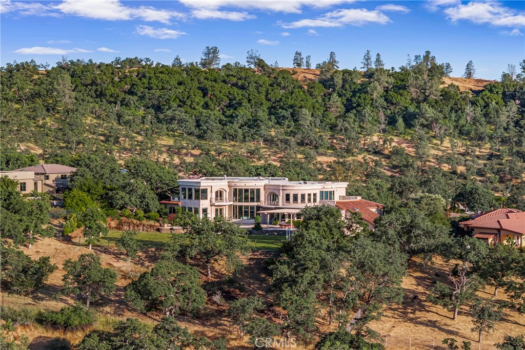 Gracefully set on 1.2 acres in the exclusive Canyon Oaks Country Club, this Mediterranean-inspired estate is a rare expression of enduring beauty and refined living. Thoughtfully envisioned by its original owners and masterfully built by renowned custom homebuilder Michael Gali, the residence captures the essence of architectural sophistication, elevated comfort, and seamless integration with its natural surroundings. Nestled along the boundary of Upper Bidwell Park, the property has direct access to the South Rim Trail, offering unobstructed entry to Chico’s most iconic landscapes. A welcoming circular driveway, gracefully created with granite pavers, winds through the property and sets the tone for a truly unforgettable arrival. An inviting storybook-style balcony, poised beside a majestic covered entrance, evokes the feeling of timeless grandeur. Inside, a dramatic foyer reveals soaring ceilings, a sweeping spiral staircase, and radiant light dancing across Italian marble floors. The Great Room features striking rotunda windows with panoramic canyon views, seamlessly blending the indoors with nature. The chef’s kitchen boasts all-Viking appliances, a double oven, and bespoke mahogany cabinetry. Four spacious bedrooms and four-and-a-half baths include a primary suite with private terrace, sunken palatial tub framed by marble columns, and dual showers offering floor-to-ceiling views-an unforgettable start or end to any day. An ambient mezzanine connects the home’s wings, while a richly appointed library features a fireplace, built-ins, and terrace access. A three-car tiled garage blends style with practicality. Modern amenities abound: a private theater, five fireplaces, radiant floor heating, Lutron drapes, smart lighting, surround sound, water softener, and owned solar ensure comfort and efficiency. Outdoors, enjoy a shimmering pool, multiple verandas, a poolside bath and designer shower. A separate steam room offers a luxurious spa-like escape, perfect for relaxing after a hike or a day on the green. Evenings are best savored from the rooftop terrace, where breathtaking canyon and sunset views stretch endlessly across the horizon. Whether enjoying intimate conversation under starlit skies or selecting a vintage bottle from the in-ground, temperature-controlled wine cellar, the experience is nothing short of magical—designed to elevate daily living into something extraordinary. A true haven, this sanctuary blends fine craftsmanship with timeless beauty.