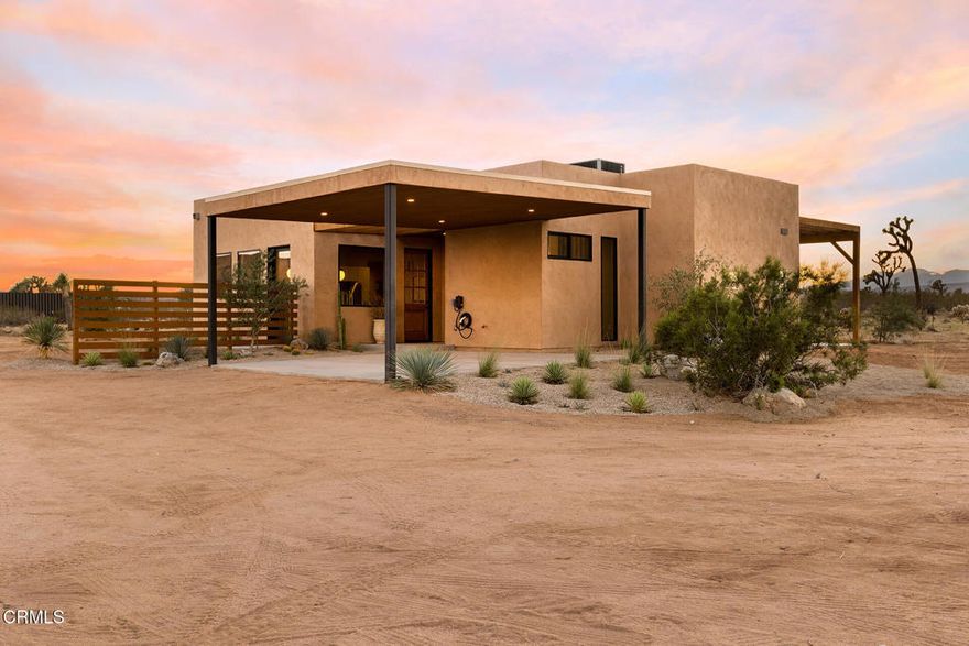 Experience elevated desert living in this new modern retreat set on over two acres in Northern Joshua Tree. Designed to frame sweeping sunset views of the San Gorgonio Mountains, this 3-bedroom, 2-bathroom home blends contemporary style with natural tranquility. Exposed aggregate concrete floors, high ceilings, and expansive sliding doors connect the light-filled interiors to the desert landscape, while the chef's kitchen impresses with Bosch appliances, a waterfall island, custom range hood, pot filler, and designer lighting. The great room separates the guest wing from the primary suite for added privacy, and each bedroom opens directly outdoors for effortless indoor-outdoor living. The primary suite offers a spa-like bathroom with floor-to-ceiling tile, skylights, and an additional outdoor soaking tub and shower for stargazing. The expansive back patio offers a space to gather around the built-in firepit or relax in the hot tub surrounded by panoramic desert views. Fully electric and energy-efficient, the home includes owned solar, central HVAC, an EV charger, and dark-sky-friendly lighting. The two-car carport can double as shaded outdoor space, while drought-tolerant landscaping with olive trees and creosotes enhances the peaceful setting. Near local favorites like La Copine, Crossroads, and Pappy & Harriet's, this thoughtfully crafted home truly captures the spirit of modern desert living.