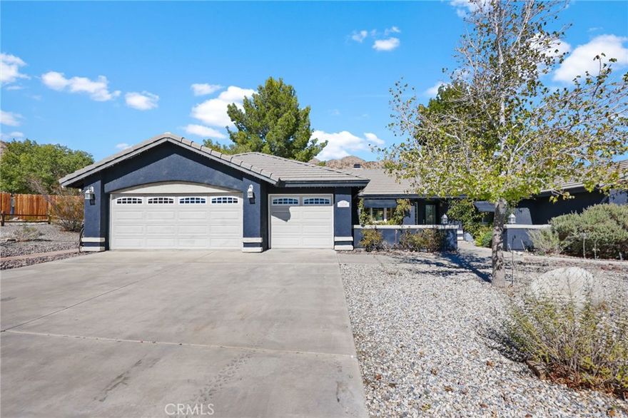 Discover desert living at its finest with this beautifully maintained single-story retreat nestled in the highly sought-after Sycamore Rocks neighborhood of Apple Valley. Situated on an expansive 28,900 square foot lot, this 4-bedroom, 2-bath home offers space, privacy, and timeless charm surrounded by breathtaking mountain views.
From the moment you arrive, the home’s inviting curb appeal and tranquil setting set the tone for what’s inside. The exterior features modern dark tones accented by light stone details, a large three-car garage, and a spacious driveway perfect for guests, RVs, or recreational vehicles. Step through the front door and you’re greeted by vaulted ceilings, abundant natural light, and an open layout designed for both everyday living and entertaining.
The living room is warm and welcoming, anchored by a beautiful fireplace and custom built-in shelving—an ideal place to gather on cool desert evenings. Adjacent is the dining area and a thoughtfully designed kitchen that combines style and functionality. With rich wood cabinetry, sleek black granite-style countertops, and stainless steel appliances, the kitchen offers ample space for preparing meals and hosting family gatherings. A decorative stained-glass pendant adds a touch of character to the open space.
The primary suite is a true retreat, featuring soaring ceilings, soft natural light, and generous room for a king-sized bed and sitting area. The adjoining bathroom offers comfort and convenience, while the additional bedrooms provide flexibility for guests, a home office, or creative spaces.
Step outside to a backyard oasis surrounded by mature trees and peaceful desert landscaping. Enjoy shaded afternoons under the covered patio or unwind while taking in the serene views of the surrounding hills. The large, level backyard transitions seamlessly into open desert terrain, offering plenty of space for a pool, garden, or future ADU. Whether you envision family gatherings, outdoor entertaining, or quiet evenings under the stars, this property delivers endless possibilities.
Located in a quiet cul-de-sac with minimal traffic, this home combines the privacy of country living with easy access to shopping, schools, parks, and local hiking trails. 20058 Rancherias Lane is more than a home—it’s a lifestyle of tranquility, space, and natural beauty in one of Apple Valley’s most desirable communities.