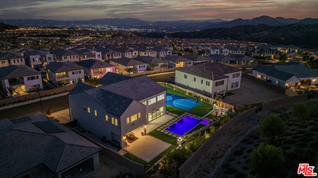 An Extraordinary Estate in Porter Ranch's Prestigious Ridge Collection. Perched high in the exclusive, guard-gated hills of Porter Ranch, this nearly new architectural masterpiece offers an elite level of luxury living with beautiful Sunset and Hillside views. Set on a one-of-a-kind, over 20,000 sq ft flat lot, this residence boasts an unrivaled resort-style backyard designed for both grand entertaining and everyday indulgence. Outdoors, you'll find a FULL BASKETBALL court, a sparkling pool & spa with cascading fountains, a fully equipped outdoor BBQ, a covered lounge patio, and a cozy fire pit area with seating for up to ten, perfect for unforgettable gatherings under the stars. Inside, the inviting entry and extended foyer lead past a sophisticated dining room into the expansive great room and casual dining area, each showcasing views of the luxurious outdoor living space. The gourmet chef's kitchen features a massive quartz-stone island with breakfast bar, abundant cabinetry, premium appliances, and a spacious walk-in pantry. The enormous primary suite is a true sanctuary, highlighted by elegant coffered ceilings, a palatial walk-in closet, and a spa-inspired bath with dual vanities, a soaking tub, a luxe glass-enclosed shower, and a private water closet. A convenient lower-level bedroom with ensuite bath is ideal for guests, while upstairs offers four additional spacious bedrooms, a light-filled loft, and a well-appointed laundry room. The 3-car garage provides ample storage and convenience. All of this is located moments from the top-rated Porter Ranch Community School (TK8), Sierra Canyon School, upscale dining, shopping, and the brand-new 50-acre Porter Ranch Park. Move-in ready NO NEED TO WAIT FOR BUILD OUT! Designed to impress this is more than a home, it's a lifestyle statement. Click the VIRTUAL TOUR link for a full video.