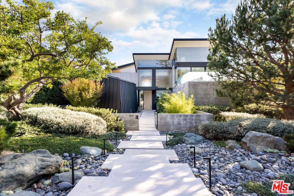 Presenting Flight, a modern yet timeless Palisades Riviera portfolio piece designed by the widely published; a visionary blueprint by highly acclaimed California architect William Hefner. A masterful fusion of high-quality materials with nods to all of earth's basic elements, this thoughtfully crafted modern marvel arrests the senses on approach. Meticulous landscaping contributes to an overall sense of calm. Warm light glows through large metal-framed walls of glass converging with smooth concrete for added contrast behind the surrounding greenery. Inside, the foyer is itself a work of art, with an accent wall of varied vertical lines illuminating the entry as globes of glass dangle overhead. Soft floor tiles mimic the wood grain of the minimalist glass-sided staircase. A refreshingly delightful powder room welcomes visitors with a dazzling display of light reflecting off of textured walls. Beyond, the living room is centered by a commanding yet reserved fireplace flanked by plush built-in seating and clerestory windows bringing natural light in. To the left, a perfectly positioned wet bar offers plenty of room for entertaining guests. Nearby, a temperature-controlled wine enclosure separates the open-concept formal dining area from the state-of-the-art kitchen. The culinary center of the home features multiple prep spaces and built-ins including butler's station and writing desk, a large center island with secondary prep sink and bar seating, glossy cabinetry, top-of-the-line stainless-steel appliances including Wolf cooktop with hood, quartz countertops, and built-in breakfast nook. Massive Fleetwood doors envelop the interior spaces, opening to provide seamless transition to the rear patios perfect for relaxing under the stars or dining al-fresco. Upstairs, the voluminous primary suite is the true prize of the home, with partial ocean views, a vaulted ceiling, sitting area, fireplace, and architecturally important clerestory windows bathing the space in light. The primary bathroom offers dual floating vanities, spa-inspired shower, and a dressing room to rival most department stores. Fleetwood doors access a private balcony which spans the entire rear of the home, overlooking the grounds below. Secondary bedrooms also include their own private patios for the ultimate indoor/outdoor lifestyle, and a front balcony can be found just outside the upstairs guest bedroom. Additional amenities include a three-story elevator, fully insulated safe room, theatre, gym, office, zen gardens, and studio/guest house. The rear yard is secluded by lush greenery and includes a pool with infinity waterfall edge, lounging deck, built-in barbecue, and plenty of grass to roam and play. This serene residence is currently being utilized as three bedrooms plus guest house but can be reconfigured as five bedrooms plus guest house. Welcome to this one-of-a-kind sanctuary just moments to Palisades Village, Malibu, beaches, and all of the plentiful shopping, dining, and entertainment Santa Monica and the Westside have to offer. Currently utilized as three bedrooms, but reconfigurable to six bedrooms.
