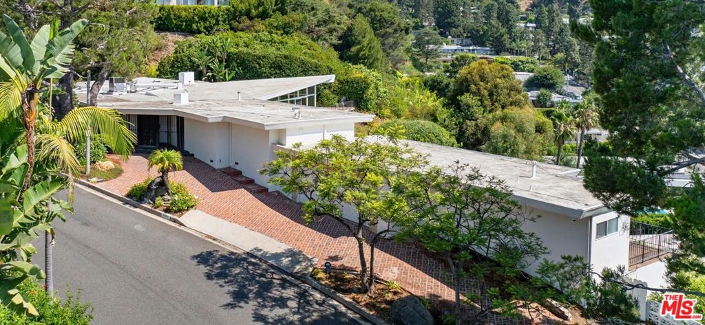 FIRST TIME ON THE MARKET IN NEARLY 40 YEARS! Steeped in rich history, this remarkable home was rumored to be owned by American socialite Marylou Whitney of the Vanderbilt family, later passing to renowned art dealer Wallace Findlay Jr., before being acquired by the present-day owner. A rare architectural gem in the heart of Trousdale Estates, this residence embodies the sophistication of mid-century modern design distinguished by its bold geometric floor plan and seamless integration with its surroundings. The home's signature triangular living room commands city views, framed by walls of glass that bathe the interior with natural light. Located at the heart of the home is the dramatic circular 'Great Room' which serves as a statement of style and scale, opening through floor-to-ceiling glass windows to an expansive backyard retreat. Here, lush landscaping surrounds a custom lava-rock waterfall and resort-style pool, creating a private sanctuary designed for both grand entertaining and tranquil relaxation. Square footage provided by Floor Plans Pros: Main House 4,157 sqft Guest Suite 314 sqft. Probate sale, court confirmation may be required.