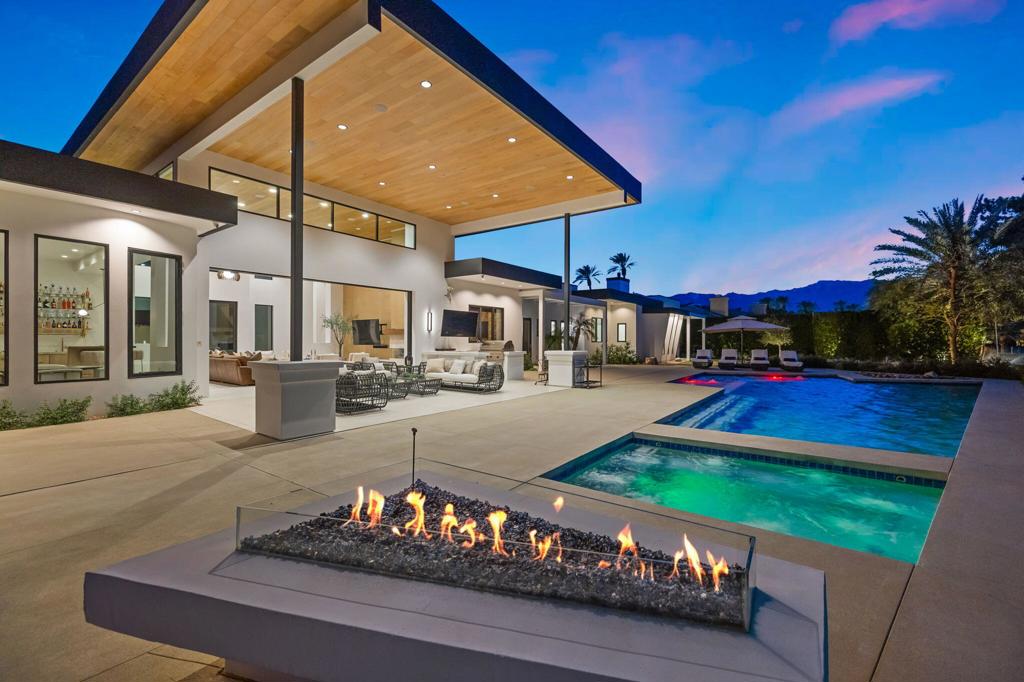 Nestled behind a private gate within the exclusive Mission Hills Country Club, this 6,830 sq. ft. contemporary masterpiece offers unparalleled design and architectural elegance. Every detail has been meticulously crafted to create a seamless blend of indoor and outdoor living. Towering 20-foot wood-lined ceilings and expansive walls of glass invite natural light while framing breathtaking double fairway views from the 12th tee of the Pete Dye course. This exceptional home features four luxurious en-suite bedrooms and five bathrooms, thoughtfully designed for both comfort and flow. The primary suite, positioned at the east end, boasts a spa-like bath with a walk-in shower, dual vanities, separate toilet areas, and a custom walk-in closet. A junior primary suite, complete with a soaking tub, shower, and dual walk-in closets, along with two additional spacious en-suite bedrooms, are located at the opposite end of the home. Art enthusiasts will appreciate the gallery-style hallways, offering ideal niches for curated collections. The home office, surrounded by glass, includes a private entrance, making it perfect for remote work or creative endeavors. Outdoors, a resort-style setting awaits with a large pool and spa, a fire pit, an outdoor kitchen with a TV, and expansive concrete decking--ideal for entertaining. Enjoy breathtaking mountain and golf course views from the covered patio, offering the perfect setting for relaxation. Designed for convenience and security, the estate includes a four-car garage, with two separate two-car garages strategically placed at opposite ends of the home. With a low HOA of just $242, this modern architectural gem is a rare find, ready for the most sophisticated buyer.