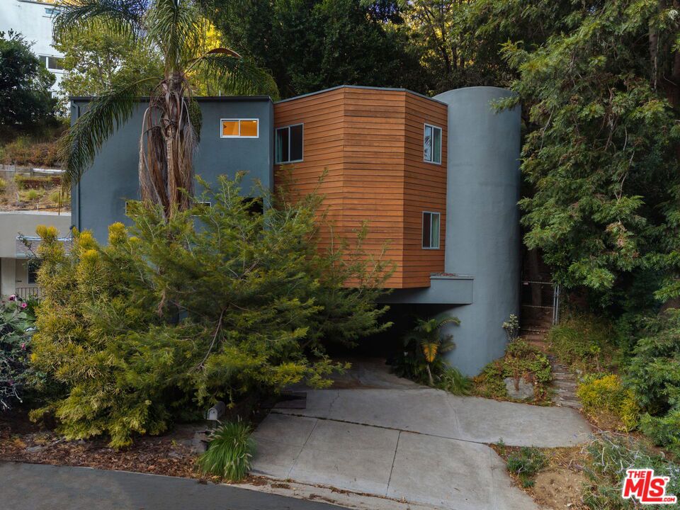 Elle Decor dubbed it "The Swankiest House in Hollywood" and it's easy to see why. Originally completed in 1978 by renowned architect Gary Gilbar and later reimagined by celebrity designers Woodson & Rummerfield, this modern masterpiece is a glamorous jewel box of style and sophistication. Behind its sleek exterior lies 3 bedrooms, 2 baths, and 1,978 sq ft of impeccably curated living space. The dramatic living and dining areas feature soaring ceilings, a statement fireplace, bold Florence Broadhurst wallpaper, and walls of glass that open to a chic entertaining deck. Outside, a tranquil terraced garden awaits, complete with a 9-foot waterfall, raised-bed vegetable garden, and Malibu lighting for magical evenings.The designer kitchen is as functional as it is stunning, boasting bi-fold lift-up cabinets, a Viking range with warming drawer, Fisher & Paykel dual dishwasher, and a built-in Miele coffee system that serves Nespresso on demand.The main level also offers a stylish guest bedroom and a fashion-forward bath. Upstairs, the spacious primary suite delivers treetop views, a high ceiling, cozy fireplace, sitting area, and a custom walk-in closet. The remodeled en-suite bath includes a dual vanity, dressing table, subway-tiled tub surround, and chic tile flooring. The third bedroom charms with custom wood bookcases and Anthropologie wallpaper.