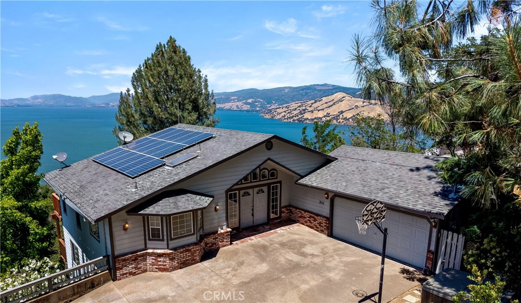Spectacular panoramic views of Clear Lake on almost a half-acre lot in Riviera Heights with OWNED SOLAR PANELS! This home features over 2,700 square feet of interior space, vaulted ceilings, an abundance of natural light, spacious decks, and ample storage. Situated between two vacant lots this property offers privacy, and magnificent lake views from almost every room. The living room provides floor to ceiling windows, a vaulted ceiling, and a freestanding pellet stove. Close by on the main level you will find the primary bedroom, with walk-in-closet, and en-suite bath. The kitchen features a dedicated dining space, eat-in breakfast counter, pantry, and half-bath. This home has an attached 2 car-garage, with direct access on the main level of the home, plus a flat and level driveway providing 3 to 4 additional parking spaces. As you make your way downstairs you are greeted by an expansive great room with mini-bar, two bedrooms, a full bath, and an oversized deck with more panoramic lake views. Extra storage is located under the lower floor with access from the side of the house. This home is located in the firewise community of Riviera Heights, which is considered to be one of the most favored communities around the lake. This HOA community offers its residents access to a marina & dock, picnic area, pool, and clubhouse available for day use. Make this home your next investment, secondary lake house, or permanent residence!