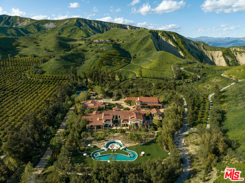 Welcome to El Palacio Del Solano, an exquisite oasis nestled within the prestigious Solano Verde Ranches. This extremely private enclave of 39 palatial estates is centrally located from Los Angeles, Malibu, & Santa Barbara. Located just 25 minutes north of Westlake Village and Thousand Oaks, and a mere 45 minutes from the pristine shores of Malibu, this secluded sanctuary offers convenience. Each of these generational estates sits on dozens of acres encompassing the most pristine natural landscapes known to Southern California. Beyond the handcrafted gates, ensconced amidst verdant fruit orchards and bordered by a meticulously manicured tree-lined driveway, awaits a truly unparalleled residence, the holy grail of Somis. Spanning 22 acres of secluded splendor, this Spanish palatial estate exemplifies opulence at every turn. Boasting approximately 20,000 square feet of meticulously designed living space, the estate epitomizes grandeur & opulence. The centerpiece is the magnificent 14,460 square foot main residence, complemented by a fully appointed 2,300 square foot guest house and an expansive 3,100 square foot hospitality and recreational facility. Step inside and be greeted by perfectly detailed Spanish tiles along the flooring and an all encompassing floor to ceiling window. From the state-of-the-art media room to the tranquil library & private office, each space exudes sophistication. Culinary delights await in the gourmet kitchen ideal for large gatherings, while the bar and wine cellar beckon for evenings of refined entertainment. Retreat to the sumptuous master suite, where a private primary living room is joined with a double-sided fireplace. The dual primary bathrooms feature a spacious dressing area, sauna, double-sided glass enclosed shower, & direct access to personal gym & office. Other notable interiors include a private massage room, arcade room, and grand formal dining room. Ascend to the second floor, where hospitality reigns supreme. Three luxurious bedroom suites, each boasting private balconies with sweeping vistas, offer unparalleled comfort. A 2nd story loft space with a bar can be found overlooking the 1st floor family room with the iconic arched window capturing the picturesque mountain views. Step into the backyard where paradise awaits. A massive grass field is accompanied by multiple lounging areas and a one-of-a-kind lazy pool with a center island fire pit. The backyard is adorned by a plethora of fruit trees including lemon, avocado, pomegranate, fig, & tangerine. Walking paths leading up to your own private mountain located to the East side of the estate offer the most scenic jaw dropping mountain views. French doors off the glass enclosed breakfast room open up to a private al fresco dining and living area accompanied by an outdoor kitchen. Multiple seating & entertainment areas allow for hosting of large dinner parties or smaller intimate events. Enjoy your own private sports court with its own shaded cabana. Start your mornings with a round of tennis or basketball. The guest house is situated with a two-car garage, two beds, two baths, fully equipped kitchen, living room, & breakfast nook. This private luxurious retreat is equipped with all living essentials. The recreational & hospitality facility are ideal for hosting the most upscale events. Tucked away behind the facility are two fully equipped restrooms. A spacious four-car garage is attached to the facility equipped with volume ceilings ideal for parking event vans, trucks, and small to mid-size buses. The possibilities are endless with regard to this facility. An estimated range of fifteen to twenty cars could comfortably be parked in the driveway and motor court spaces. Whether a notable family desires an ultra-private compound or a high-status celebrity seeks a serene oasis, El Palacio Del Solano offers a lifestyle unlike any other for the most discerning buyer.