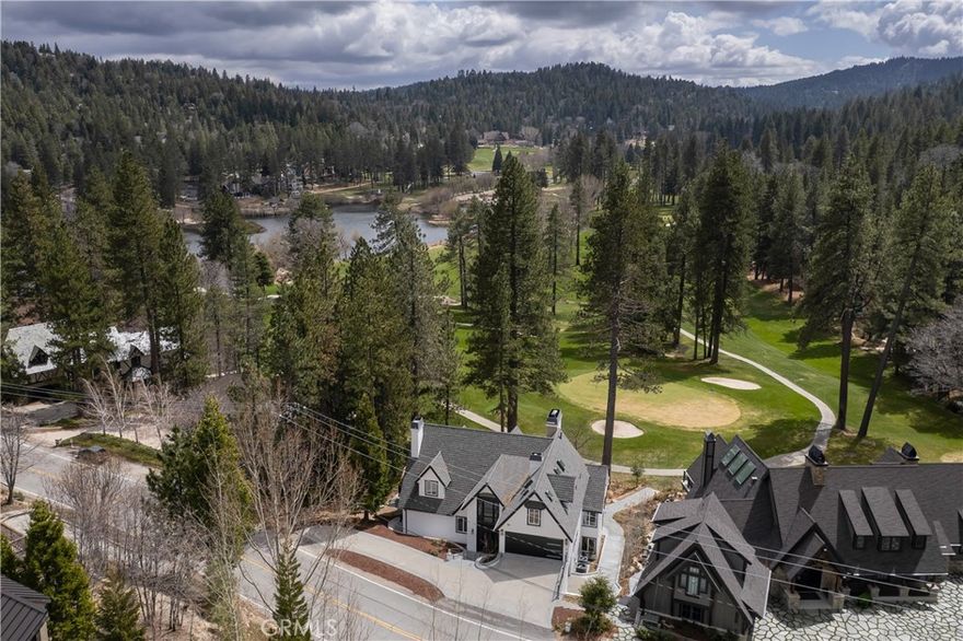 Exquisite luxury meets panoramic serenity at this fully renovated masterpiece, situated prominently on the 6th green of the prestigious Lake Arrowhead Country Club. Set within an exclusive celebrity-owned neighborhood, this residence offers unmatched views of multiple golf holes and picturesque Grass Valley Lake, with captivating vistas from every room. Meticulously redesigned, this home underwent a comprehensive renovation featuring rare and exotic finishes from RH, Arhaus, and Schoenbeck. Step into a formal foyer accented by wide plank hardwood flooring extending across the main level. The open floor plan integrates a sophisticated dining space with a gourmet kitchen, showcasing an oversized marble-topped island, Arabescato marble slab backsplash, Sub-Zero refrigerator, Wolf stove, four Wolf ovens, Cove dishwasher, drawer microwave, and elegant RH hardware. Breathtaking floor-to-ceiling windows illuminate the main living room, crowned by a striking authentic deer antler chandelier, custom cabinetry, and integrated smart home system operated via strategically placed iPads. The adjacent octagonal room offers remarkable golf views, perfect as an office or creative sanctuary. The main-level primary suite is a private retreat with vaulted ceilings, a luxurious stone fireplace, deck access, custom walk-in closet, and an opulent spa-like bathroom featuring heated floors, expansive Kohler-equipped shower, opulent $7,000 bidet toilet, and a custom Opal White Granite illuminated bathtub wall. The expansive weatherproof tile deck—over 1,000 sq ft—extends seamlessly from the office to the primary suite, ideal for entertaining or relaxing. A mudroom, emerald-accented powder room, and golf cart garage complete this level. Downstairs, a spacious game room boasts a stacked-stone fireplace, adjacent octagonal poker nook, and flexible space suitable for entertainment or theater. Additional accommodations include three bedrooms, two baths, a second primary suite with fireplace and luxe bath, plus laundry facilities. A rare golf-level patio with spa, bridge access to the course, and substantial entertaining space mirrors the upper deck’s allure. The top level presents another vaulted-ceiling primary suite with fireplace, lofted bonus area, and luxurious bath. Opposite, discover a two-story wellness haven featuring a Clearlight sauna and gym/yoga studio convertible to additional sleeping quarters. Completed by a two-car garage and a sweeping driveway.