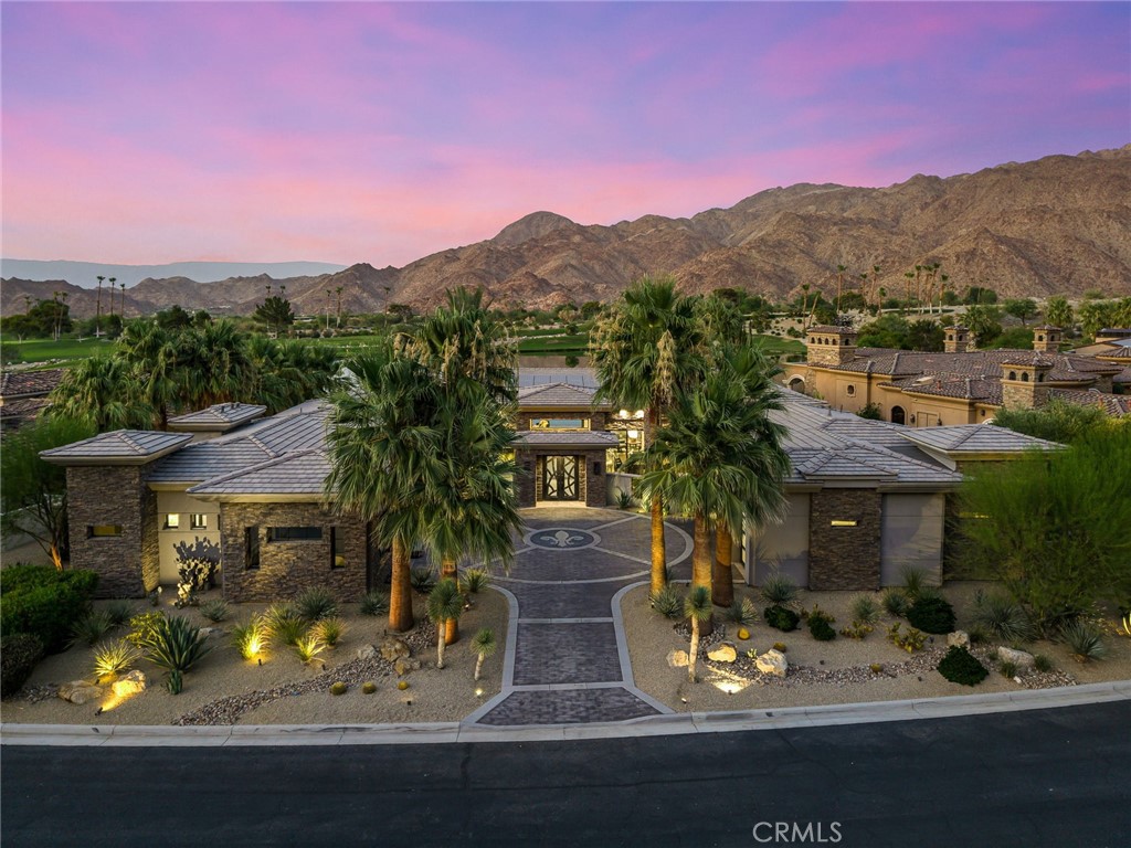 Set on one of the most exclusive vantage points in Ironwood Country Club, this residence captures the true essence of desert serenity. Walls of glass frame uninterrupted vistas across a reflecting lake, the rolling fairways of the two championship courses and to the rugged ridgelines of the Santa Rosa and Chocolate Mountains. At night, tranquility reigns with star filled skies, the radiant hush of the desert, and glowing panoramas that create a natural masterpiece.
The home spans 6,265 square feet across a private 19,600-square foot lot, designed with a modern, organic, desert centric architecture that blends seamlessly with its natural surroundings. An elegant motor court, framed by palms, water features, and desert landscape welcomes you home. Inside, refined living spaces and walls of glass with 14 foot ceilings open to breathtaking views at every turn. A modern, entertaining kitchen with seating for many, a butler’s pantry with coffee bar, a mountain view dining room, a 1,500-bottle wine room, a private viewing room with huge pivot doors, and a gym, all elevate your everyday living. Each of the four ensuite bedrooms offers its own retreat, including a luxurious private casita with a spa-inspired bath with waterfall shower. The primary suite enjoys exceptional views, two walk-in closets, fireplace, sitting area, and direct access to the pool and spa—perfect for savoring desert nights in solitude.
Ironwood Country Club is a private, member-owned community cradled by the Santa Rosa and San Jacinto Mountains National Monuments. Just moments from El Paseo yet worlds away in ambiance, this rare offering combines natural beauty, ultimate privacy, and a lifestyle defined by peace, exclusivity, and awe-inspiring desert landscapes.