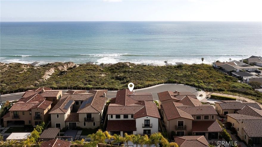 From the historic San Clemente Pier to Dana Point’s sculpted Headlands and the distant silhouettes of Catalina Island, sweeping panoramic views of the Pacific form the ever-changing backdrop to this custom-caliber residence—an elevated offering within the Azure Viewpoint Collection at Sea Summit in San Clemente. Ideally positioned on a single-loaded cul-de-sac framed by protected coastal bluffs, canyon trails, and the raw beauty of preserved open space, the Mediterranean-inspired home welcomes with a covered front patio and fireplace, extending into a sun-drenched ocean-view terrace wrapped in curated hardscaping and lush landscape design. Inside, an expanded floorplan of approximately 4,880 square feet unfolds with quiet grandeur—offering four ensuite bedrooms and four-and-one-half baths, including a refined main-level suite. Soaring ceilings, wide passages, and disappearing walls of glass create a seamless dialogue between indoors and out, with custom built-ins framing the great room’s fireplace and carrying into a dining room that connects effortlessly to both the backyard and an exquisitely appointed kitchen. The kitchen itself is magazine-worthy: a generous quartz island with seating for six, white Shaker cabinetry, artisan tilework, dual pantries—including a walk-in with integrated beverage station—and professional-grade appliances by Sub-Zero, Wolf, and Asko. A dramatic staircase, anchored by a custom desk niche, leads to a sunlit landing, versatile bonus room, and a serene primary suite where a covered balcony captures the horizon. The suite offers a retreat-like sitting area, boutique walk-in closet with direct laundry access, and a spa-like bath with freestanding tub, dual-entry shower, and uninterrupted views of whitewater and sky. Outside, a private loggia, cascading spa, open-air fireplace, and built-in BBQ kitchen complete the home’s outdoor experience—crafted for unforgettable entertaining. Built by acclaimed luxury builder Taylor Morrison, this residence enjoys access to the exclusive Summit Club, a 21,000-square-foot coastal haven with ocean-view pool, spa, fitness center, and entertaining lounge. The Sea Summit lifestyle also includes award-winning schools, access to trails and beaches, and proximity to the shops and dining of the Outlets at San Clemente.