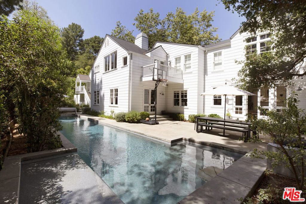 Located in the sought-after Coldwater Canyon, 2121 Trently Lane rises through the pines like a lighthouse. Though the glitter and glamour of Rodeo Drive are only minutes away, this airy, elegant compoundset on two separate parcels of landis a tranquil oasis on the edge of the city. Set behind a gated courtyard, this 4,595-square-foot home welcomes you with tasteful East Coast charm. The thoughtful floor plan blends high ceilings with well-defined spaces to create a warm, traditional setting. Abundant natural light fills the home, while beautiful upgrades cater to the most discerning buyer. Settle in at the bright breakfast bar beneath the chef's kitchen skylight, and peer through the glass-walled fireplace into the living room. Beyond the kitchen, living spaces, and dining room, the main floor includes a home office, a media room, and an ensuite library that could serve as an additional bedroom. Upstairs, the commanding primary suite features soaring ceilings and walls of windows overlooking the surrounding greenery. The spacious primary bath, complete with a Juliette balcony, is elegantly appointed with marble countertops and flooring, subway tile, and stainless steel farmhouse-style faucets. Two additional upstairs bedrooms each include ensuite bathrooms, walk-in closets, and built-in window benches that make the most of the peaceful views. A loft area completes the upper level, offering the perfect retreat for study or relaxation. Above the detached two-car garage is a large studio with its own bathroom ideal for a private office, spacious home gym, or guest suite. Step outside through chic, glass-paneled doors to enjoy the 54-foot, extra-wide lap pool, dine alfresco on the patio, fire up the outdoor grill station, or lounge across the expansive private grounds just shy of an acre and accented by oak, olive, and citrus trees. Just a stone's throw away, you'll find direct access to exceptional hiking and recreation at Franklin Canyon Park. This unique property offers the best of Beverly Hills living combining convenient city access with the serenity of an ultra-private retreat. This is one you won't want to miss.