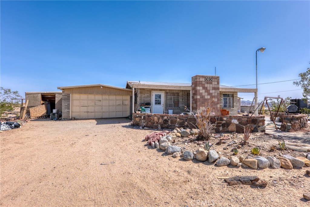 Opportunity knocks in the high desert! Set on a sprawling 5-acre corner lot just minutes from the entrance to the Marine Corps base, this 2-bedroom, 1-bath home is brimming with potential and character. Built in 1956, the home exudes vintage desert charm with vaulted ceilings, classic block and brick construction, and a striking rock archway that beautifully frames the transition from the living room to the kitchen. The cozy home is ready for a creative vision and some much-needed TLC to bring it back to life. Home has city water and power.
Step outside and imagine the possibilities—surrounded by concrete patios, the home offers a covered front porch perfect for morning coffee or stargazing at night. A detached two-car garage provides ample storage or workshop potential, and the separate block-built shed adds even more flexibility. With its south-facing orientation and wide-open desert views, the property is ripe for transformation—whether you're dreaming of a rustic desert retreat, an income-generating rental, or a long-term hold.
Located in the heart of the Morongo Basin, a region celebrated for its surreal landscapes, vibrant art scene, and close proximity to Joshua Tree National Park, this property offers both seclusion and accessibility. Bring your tools, your imagination, and your ambition—this is your chance to invest in the magic of the Mojave.