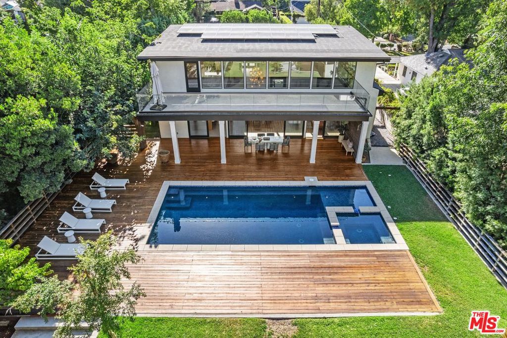 Newly constructed in 2019, this custom architectural masterpiece blends striking design with resort-style living in the heart of College Acres, one of the most coveted neighborhoods in Woodland Hills. Set on an expansive 18,000+ sq ft lot, this 5,034 sq ft home offers 5 bedrooms and 4 baths, thoughtfully designed for both entertaining and everyday comfort. A dramatic atrium entry introduces soaring 24' ceilings in the family room, seamlessly connecting to the open-concept chef's kitchen and a wall of glass that frames the entertainer's dream backyard. Outside, enjoy a heated swimmer's pool with oversized spa, a sprawling wood deck, and a garden structure with 14' ceilings, perfect as a creative studio, play space, or entertaining area. The home's versatile layout includes a loft workspace with a spacious balcony overlooking the grounds, expansive walls for art display, and multiple areas that inspire both productivity and relaxation. The primary suite is a true sanctuary, featuring dual walk-in closets, a spa-inspired bath with steam sauna, and luxurious finishes throughout. Two additional en-suite bedrooms offer private climate controls, while two flexible bedrooms can double as home offices with oversized glass doors opening to a tranquil Zen patio. Additional highlights include a full-size laundry room, direct-entry oversized 2-car garage, and a double-gated circular driveway accommodating up to 8 cars. This stunning, gated "Candy Cane Lane" residence defines the very best of SoCal living, where modern design meets comfort, privacy, and endless opportunity for entertaining.