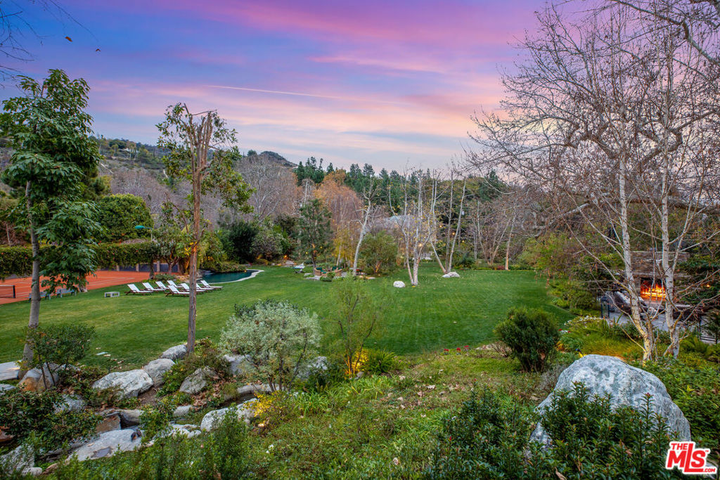A tranquil hideaway amid the graceful curves of Mandeville Canyon, this sun-drenched 1.654-acre stunner is ideal for savoring the splendors of LA's quintessential indoor-outdoor way of life. Located on a secluded corner with three separate entrances, and sharing only one lot line with a neighboring parcel, this compound offers a once-in-a-lifetime opportunity to reimagine the existing ranch-style home or build the estate of your dreams. The exquisite grounds boast a lap pool, a second adjacent swimming pool, soothing waterfalls, and hedged clay tennis court, while an oversized park-like lawn serves as a gorgeous backdrop for hosting celebratory soirees or favorite family sports. Entertain under the stars or beneath blue skies in the generous outdoor barbecue area with wood-burning fireplace. Relish in the calm of your private oasis where you can connect with nature or lose yourself among winding stone paths, hidden ponds and serene waterfalls. The charming ranch-style home includes 5 bedrooms, and is embellished with exposed-beam ceilings, a sun porch, kitchen with skylight over center island, and primary bedroom with attached sitting area and stone fireplace. Welcome your friends and loved ones with ease in the two luminous guesthouses, each with its own personal entrance. These one-of-a-kind grounds are accentuated with flourishing greenery and fruit trees - many of which line the perimeter for ultimate privacy. The flat land is rich with possibility - an outstanding opportunity to remodel or build new. Made up of three parcels, one also has the ability to subdivide into three large lots. This one-of-a-kind hideaway is a must-see for discerning buyers seeking respite from the city.