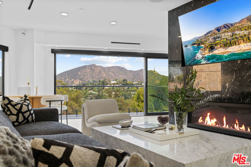 Elevated above Mulholland Drive in the Hollywood Hills, this architectural home showcases unobstructed views of the city lights, surrounding mountains, and the iconic Hollywood Sign. Designed for both relaxation and entertaining, the home features a seamless open floor plan with expansive sliding glass doors that invite natural light and breathtaking sunsets. The open-concept interiors feature a chef's kitchen with professional-grade appliances, an expansive island, and effortless flow into the living and dining spaces. The primary suite is a private sanctuary with a balcony, sitting area, custom walk-in closet, and a spa-level bath with soaking tub, glass-enclosed shower, heated floors and European finishes. Equipped with state-of-the-art Crestron smart home automation, the residence offers effortless control of automatic shades, multi-room speakers, dimmable lighting, climate, and security all from your device. For music enthusiasts, a professional-grade recording studio with full soundproofing provides the perfect environment to create and produce with ease. Additional features include fruit trees, and a reverse osmosis water system delivering purified alkaline water straight from the tap. With striking curb appeal, a beautifully landscaped front yard, a two-car garage, EV charging, and a desirable location just moments from Runyon Canyon, the Hollywood Bowl, and the Sunset Strip, this residence embodies modern luxury in one of Los Angeles' most iconic settings.