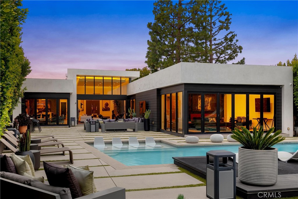 Breathtaking Modern Oasis in the Hollywood Hills. This exceptional 4-bedroom, 5-bathroom contemporary residence sits perched in the prestigious Hollywood Hills, offering unparalleled views of the Griffith Observatory, iconic Hollywood Sign, and San Fernando Valley. The sophisticated one-story design showcases clean architectural lines with a perfect balance of white stucco and dark accent walls. Step inside to discover an airy, open concept living space. Floor-to-ceiling glass walls flood the interior with natural light while framing the spectacular views. The elegant living room features a comfortable, light-colored sectional, perfect for entertaining or relaxing while taking in the scenery. The gourmet kitchen boasts sleek cabinetry, premium appliances, and a stylish island with bar seating that opens to the main living areas. The carefully curated neutral palette throughout the home creates a calm, sophisticated atmosphere. Multiple sliding glass doors blur the boundary between indoors and out, leading to an entertainer's paradise with several distinct outdoor living spaces. The expansive concrete paver patio surrounds a striking swimming pool with in-water loungers. Multiple seating areas, including a cozy fire feature, provide perfect spots to enjoy the breathtaking sunsets and night views. The thoughtfully designed landscape showcases drought-tolerant plantings, mature trees, and architectural succulents that complement the home's modern aesthetic while requiring minimal maintenance. Additional features include a detached studio, epoxy-finished garage floor, and meticulously maintained grounds that create a private sanctuary in one of Los Angeles' most coveted neighborhoods.