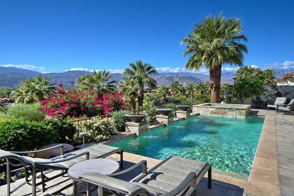 This spacious Plan 923 inside Toscana Country Club offers modern desert living and stunning views of the lake, mountains, and Hole 16 of the Jack Nicklaus Signature North Golf Course. Luxury details of this home include soaring pocket doors that blend indoor-outdoor living, a huge wetbar with butted-glass windows for maximum views, two fireplaces in the great room + one in the primary bedroom and one in the courtyard, a formal dining space that's open to the great room and kitchen, a custom pool and spa with water features, and more.The open floorplan is perfect for entertaining while still maintaining designated lounge, bar, dining, and pool table areas. The gourmet kitchen offers gorgeous granite counters atop ample cabinetry, including an island and separate breakfast bar peninsula. The massive hood over the six-burner + griddle range and the panel-matched refrigerator add a sleek aesthetic.Relax in the primary bedroom, featuring a granite fireplace surround, and an en-suite bath that offers a large freestanding soaking tub, separate sinks and vanities, walk-in closet, and massive walk-in shower. The guest house provides a large great room and separate bedroom + en-suite bath, and includes a kitchenette with dining area. Guests may also enjoy either of the two main-home guest rooms with en-suite baths.