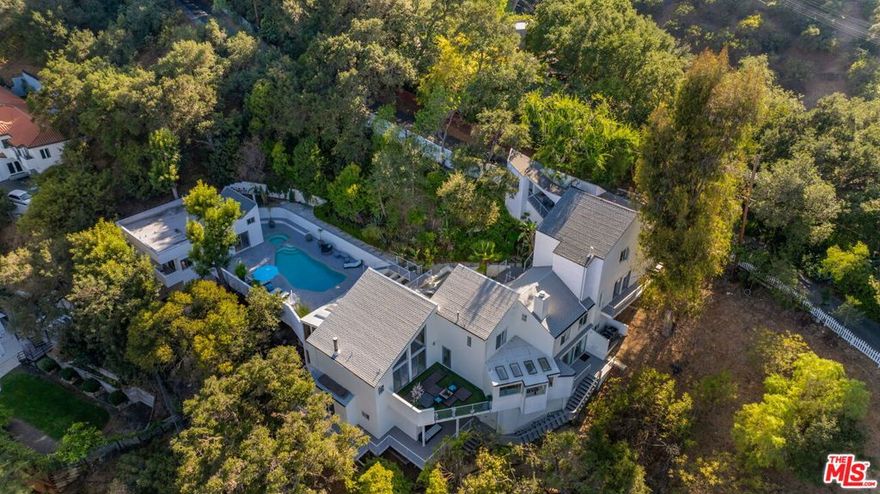 A secluded hillside compound with sweeping views, 3210 Coldwater Canyon Lane offers a rare blend of privacy and light-filled living. Spanning 27,000 square feet across two structures and three levels, the property balances airy interiors with lush outdoor spaces.The 4,400-sq-ft main residence opens to an expansive floor plan where walls of glass frame decks, gardens and a sparkling nine-foot pool with an oversized spa. Recently refreshed, the kitchen pairs new white-quartz counters and skylights with Thermador appliances, while soaring ceilings elevate the living and dining areas. Two lofted spaces invite creative use. Six ensuite bedrooms include a dramatic primary suite with fireplace, blackout shades and a spa bath featuring a sculptural round tub. Each secondary suite enjoys its own deck and captivating views.Across the pool deck, a 1,200-sq-ft guest house offers a full kitchen, living room, laundry and two additional ensuite bedrooms, ideal for visitors, work or retreat. Mature gardens wrap the pool terrace, where palms, rosemary and hundreds of exotic plantings create a private oasis.Positioned between Beverly Park and The Summit, this enclave has long attracted artists and icons seeking privacy near Beverly Hills and Studio City. With hiking trails close by and easy access to dining, shopping and studios, Coldwater Canyon Lane embodies the best of California living.