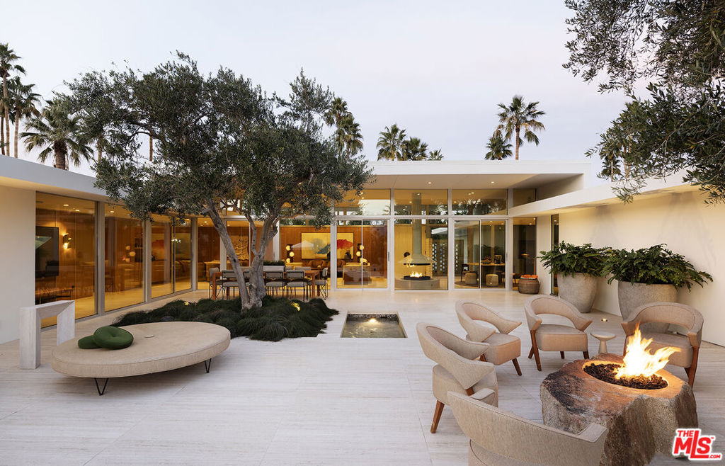 Perfectly situated on the renowned Tamarisk Country Club golf course, this timeless mid-century gem by architect Val Powelson offers panoramic views of the San Jacinto mountains. Originally built in 1959, it has undergone a recent creative reimagination and restoration by design-build firm Studio Veren. Featured in the November 2024 issue of Palm Springs Life Magazine, this four-bedroom (all ensuite), four-and-a-half-bath home seamlessly blends mid-century modern architecture with contemporary luxuries, creating the perfect home for nesting or entertaining. The home was built with entertaining at its heart, featuring an elegant flow that encourages hosting both indoors and out. Imported travertine slab flooring is throughout the home, running seamlessly into the outdoor living areas. The warmly paneled living area with its wall of glass is anchored at one end with a custom floating fireplace and a fully outfitted built-in bar at the other. The kitchen, designed not to look like a typical kitchen, satisfies any chef with its 48" Dacor dual fuel range with steam oven, tower refrigerator and freezer, oversized island, coffee bar, and custom walk-in pantry. Conveniently located off the kitchen is an outdoor BBQ patio with the built-in Lynx grill, seating area surrounded by citrus trees. The guest bedrooms, separated from the primary, are almost too comfortable with their own luxury baths, individual HVAC controls, Sonos sound systems, and private patios. The attached casita with its own entrance offers privacy and makes for a perfect office or guest suite. With its wall of glass, the primary suite has some of the best views in the house. The primary bath has custom integrated marble sinks, custom mirrors, a glass-walled shower with mountain views, electronic bidet, heated floors, and of course an outdoor shower garden. The walk-in closet even has a built-in steamer/sanitizer. Step into the lush resort-like outdoor spaces perfect for lounging, entertaining, and taking in the California sun. Anchored by a uniquely shaped pool and spa, which is tucked behind an impressive grove of cactus, you'll also find a dining area with seating for 10, a tranquil water feature, and 2 lounge areas each with their own fire feature. The property is walled and gated ensuring privacy and security and features a wired camera system, Control4 Home automation, and surround sound throughout the home/property. Also included are owned solar and a Tesla back-up powerwall. This rare find is available turn-key and fully furnished.