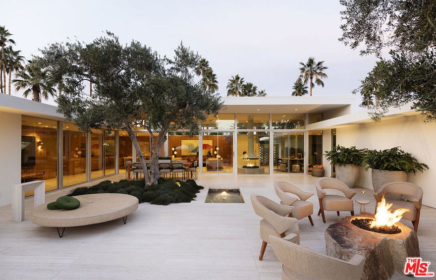 Perfectly situated on the renowned Tamarisk Country Club golf course, this timeless mid-century gem by architect Val Powelson offers panoramic views of the San Jacinto mountains. Originally built in 1959, it has undergone a recent creative reimagination and restoration by design-build firm Studio Veren. Featured in the November 2024 issue of Palm Springs Life Magazine, this four-bedroom (all ensuite), four-and-a-half-bath home seamlessly blends mid-century modern architecture with contemporary luxuries, creating the perfect home for nesting or entertaining. The home was built with entertaining at its heart, featuring an elegant flow that encourages hosting both indoors and out. Imported travertine slab flooring is throughout the home, running seamlessly into the outdoor living areas. The warmly paneled living area with its wall of glass is anchored at one end with a custom floating fireplace and a fully outfitted built-in bar at the other. The kitchen, designed not to look like a typical kitchen, satisfies any chef with its 48" Dacor dual fuel range with steam oven, tower refrigerator and freezer, oversized island, coffee bar, and custom walk-in pantry. Conveniently located off the kitchen is an outdoor BBQ patio with the built-in Lynx grill, seating area surrounded by citrus trees. The guest bedrooms, separated from the primary, are almost too comfortable with their own luxury baths, individual HVAC controls, Sonos sound systems, and private patios. The attached casita with its own entrance offers privacy and makes for a perfect office or guest suite. With its wall of glass, the primary suite has some of the best views in the house. The primary bath has custom integrated marble sinks, custom mirrors, a glass-walled shower with mountain views, electronic bidet, heated floors, and of course an outdoor shower garden. The walk-in closet even has a built-in steamer/sanitizer. Step into the lush resort-like outdoor spaces perfect for lounging, entertaining, and taking in the California sun. Anchored by a uniquely shaped pool and spa, which is tucked behind an impressive grove of cactus, you'll also find a dining area with seating for 10, a tranquil water feature, and 2 lounge areas each with their own fire feature. The property is walled and gated ensuring privacy and security and features a wired camera system, Control4 Home automation, and surround sound throughout the home/property. Also included are owned solar and a Tesla back-up powerwall. This rare find is available turn-key and fully furnished.
